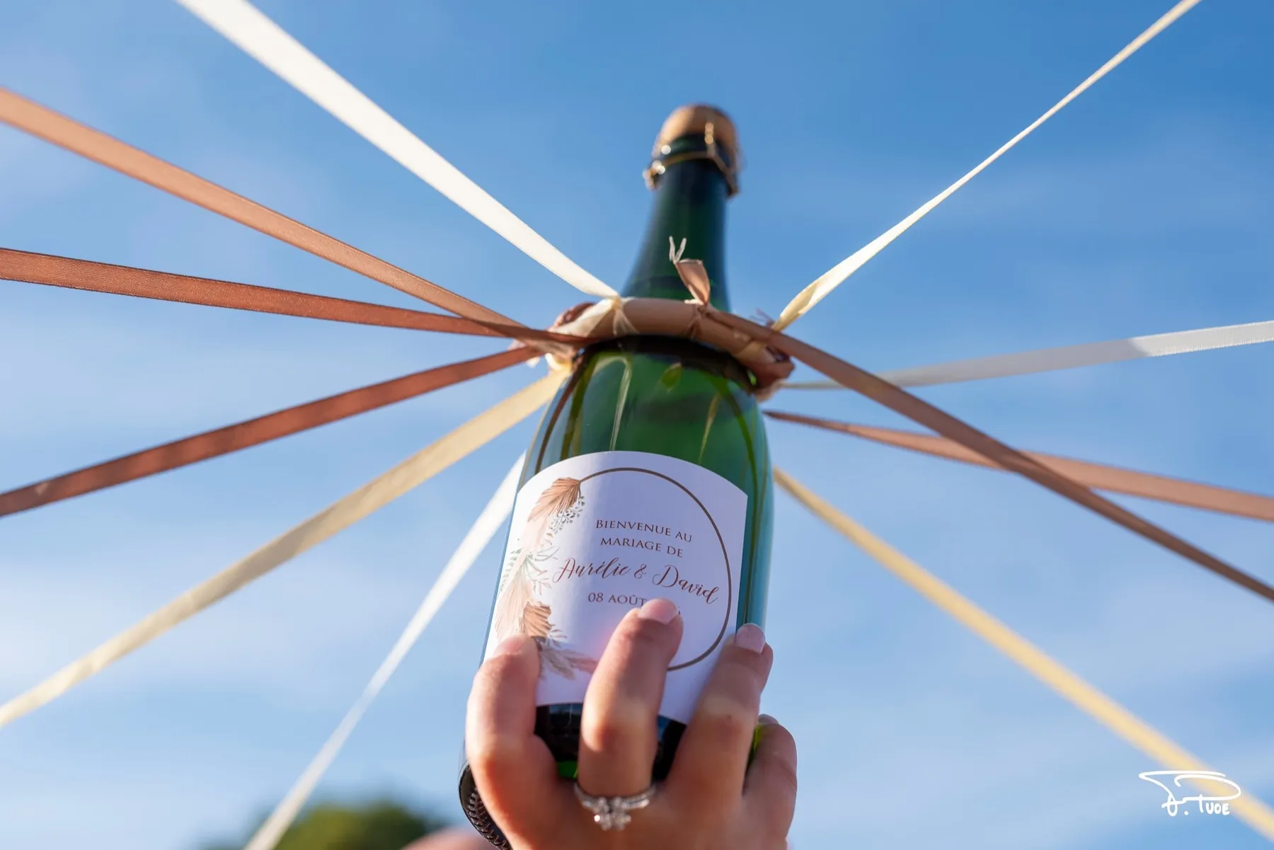 Une bouteille de champagne tendue vers le ciel, reliée à des rubans