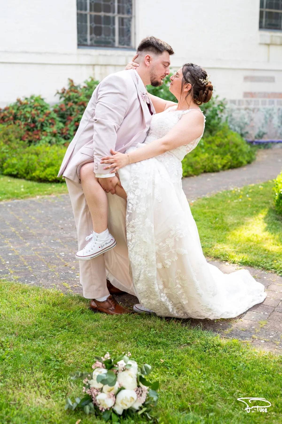 Le marié embrasse la mariée qui lève la jambe dans ses bras, dans un jardin