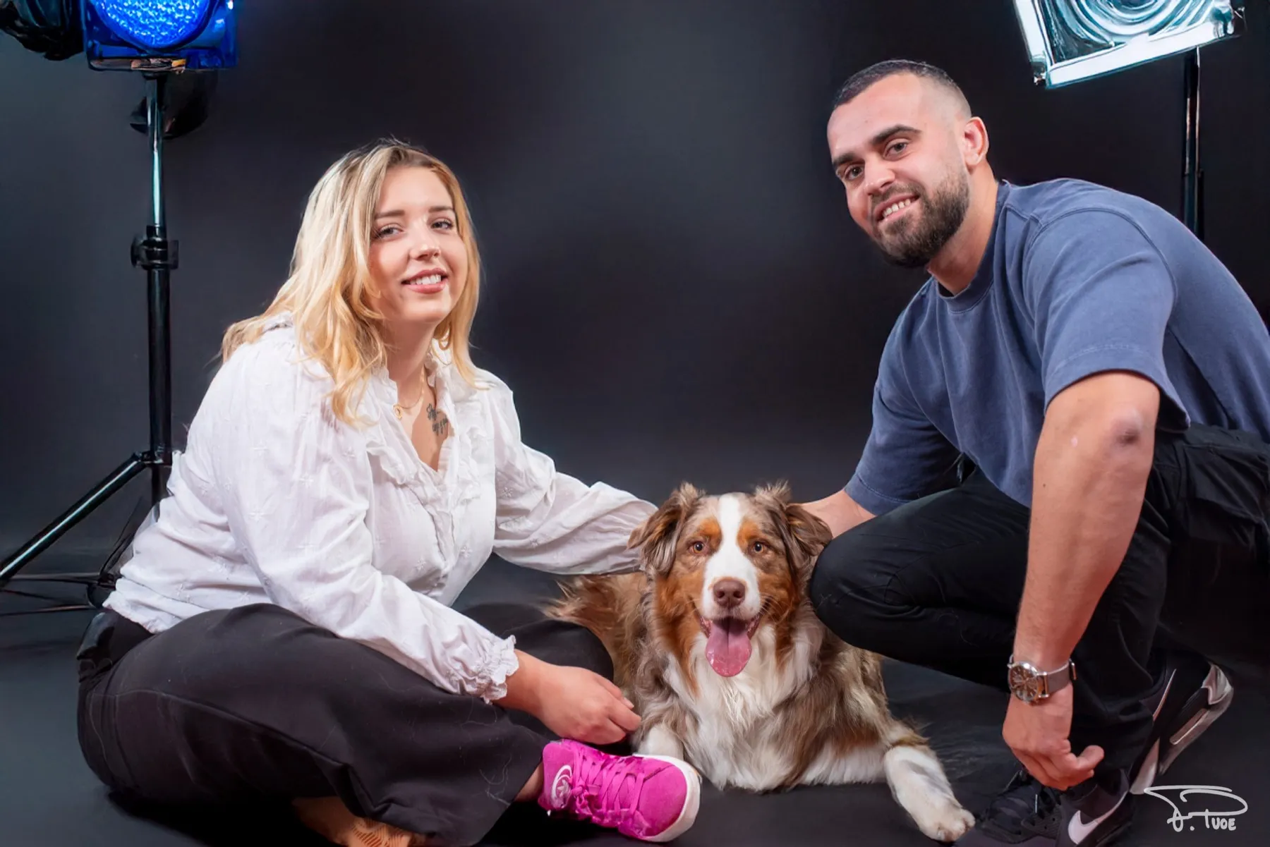 Un couple assis par terre avec leur chien, sur fond noir en studio