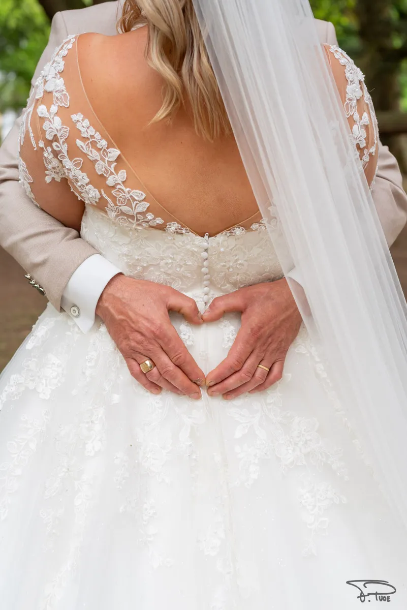 Le marié forme un cœur avec ses mains sur le dos en dentelle de la mariée