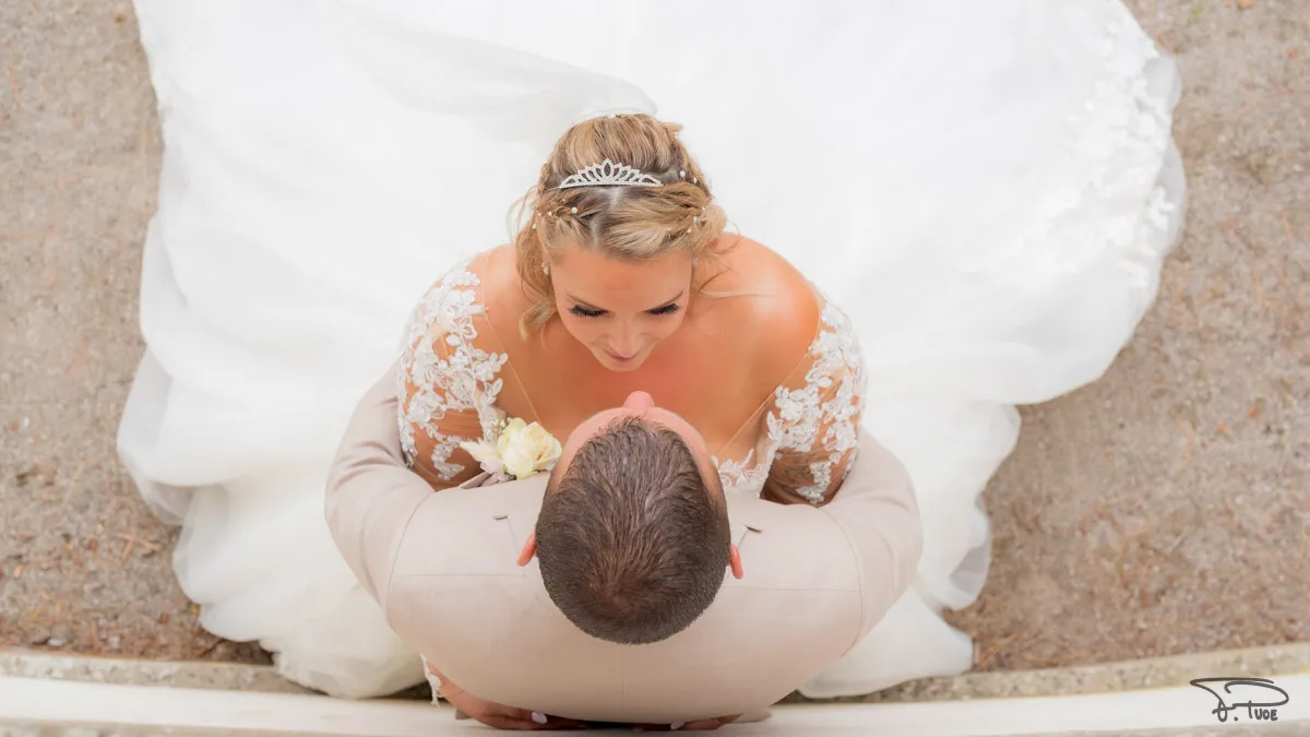 Vue de dessus, la mariée assise sur sa robe embrasse le marié