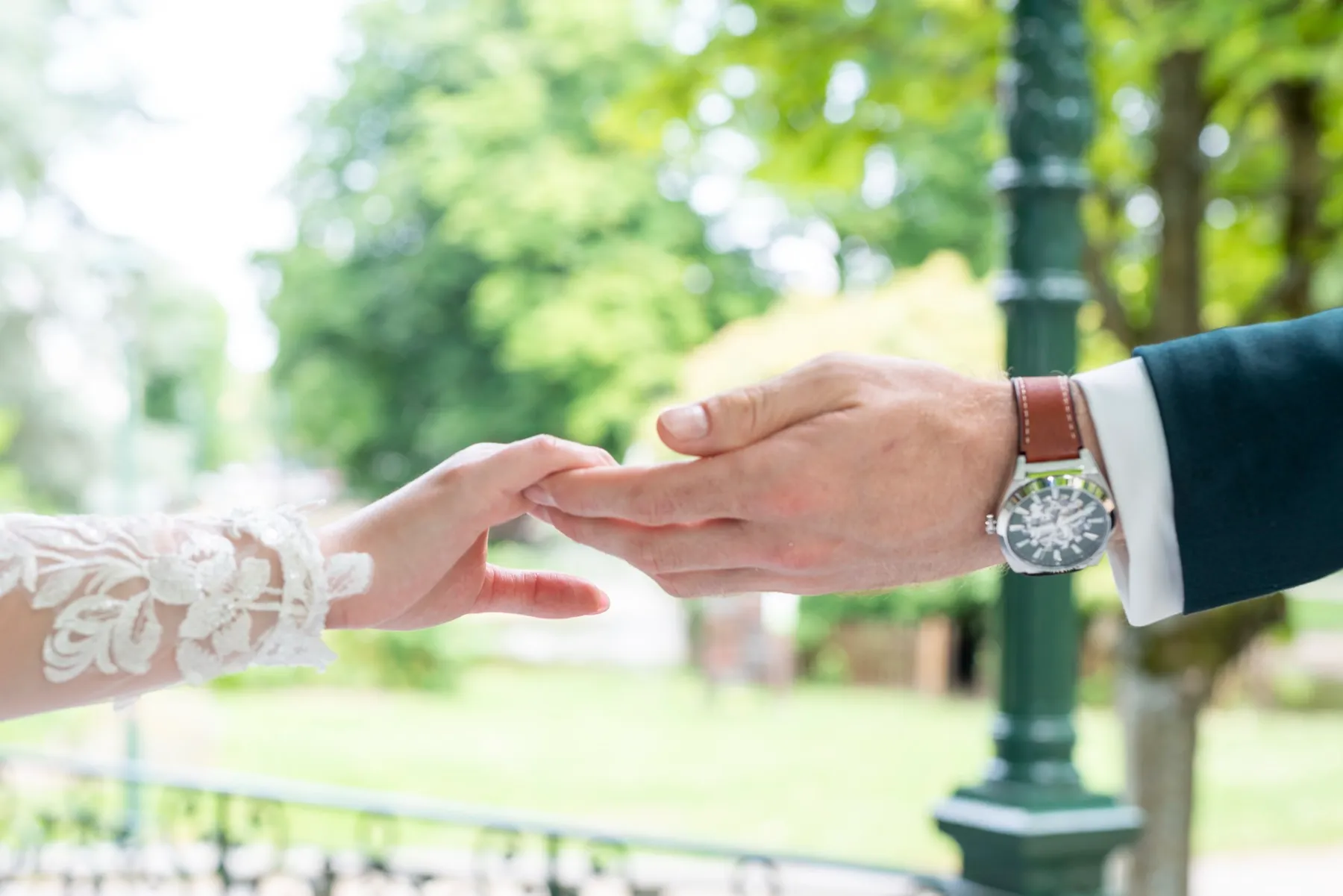 Les mains des mariés se tendent l’une vers l’autre dans un parc
