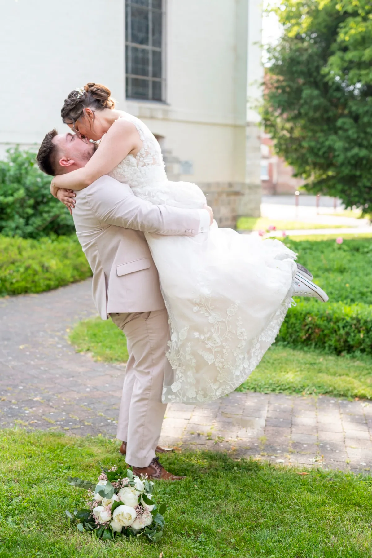Le marié soulève la mariée pour un baiser dans le jardin devant l’église