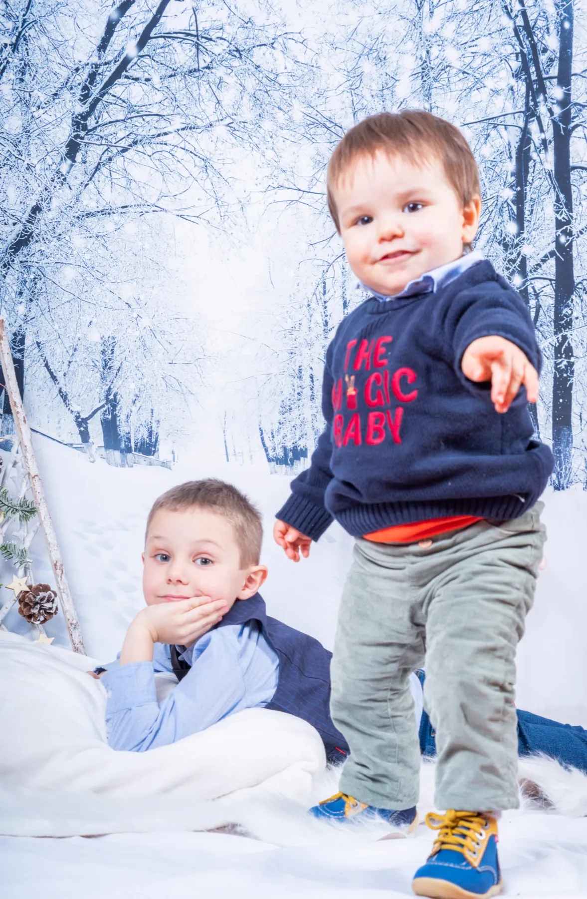 Deux petits frères devant un décor de forêt enneigée en studio, le plus jeune debout pointe l’objectif du doigt