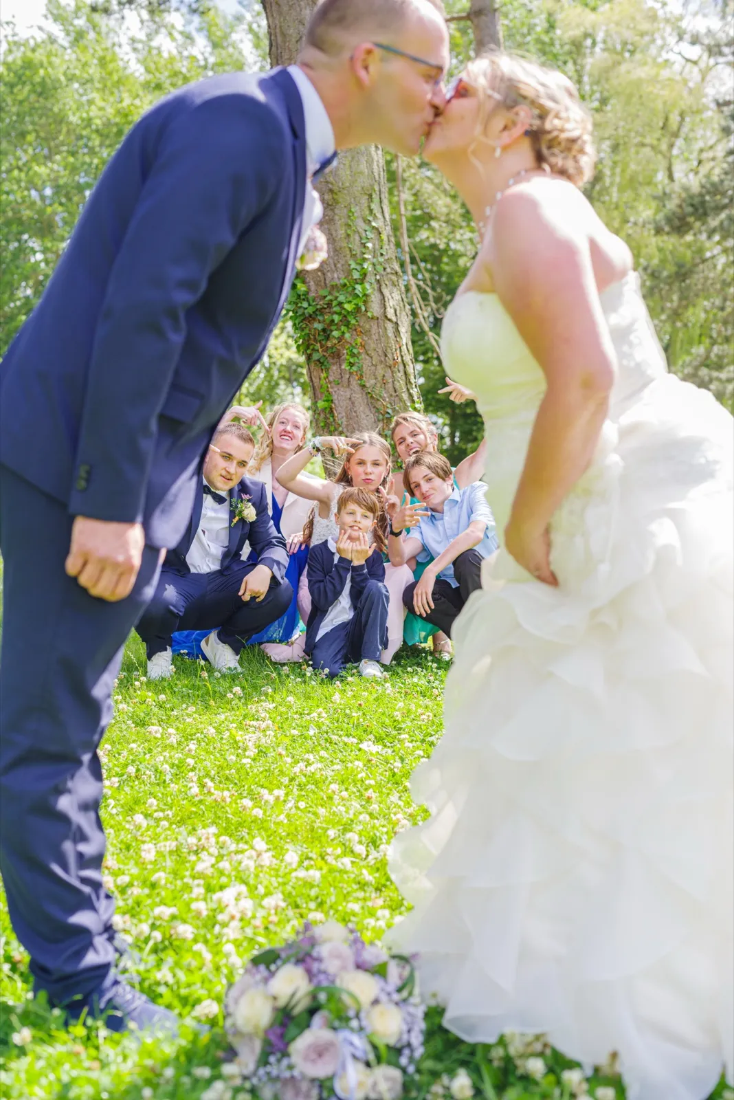 Les mariés s'embrassent debout dans l'herbe tandis que des enfants grimacent derrière eux