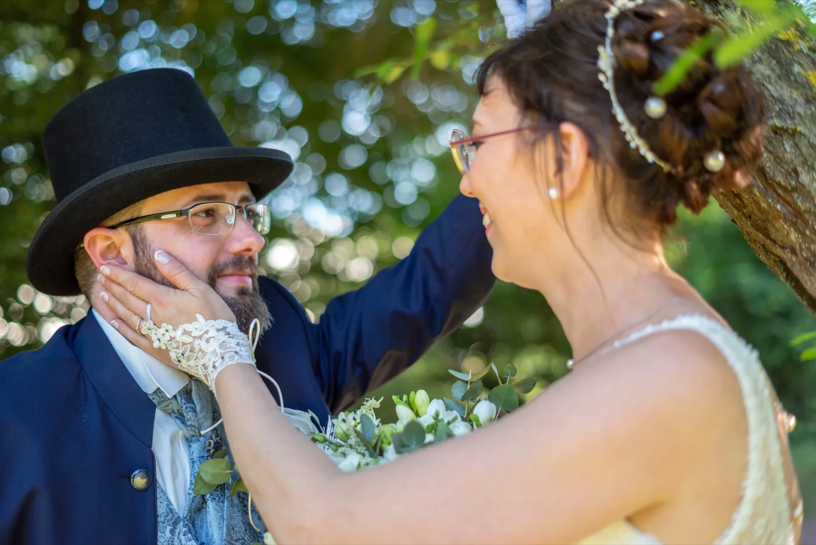 La mariée pose sa main gantée sur la joue du marié en haut-de-forme, tous deux souriants