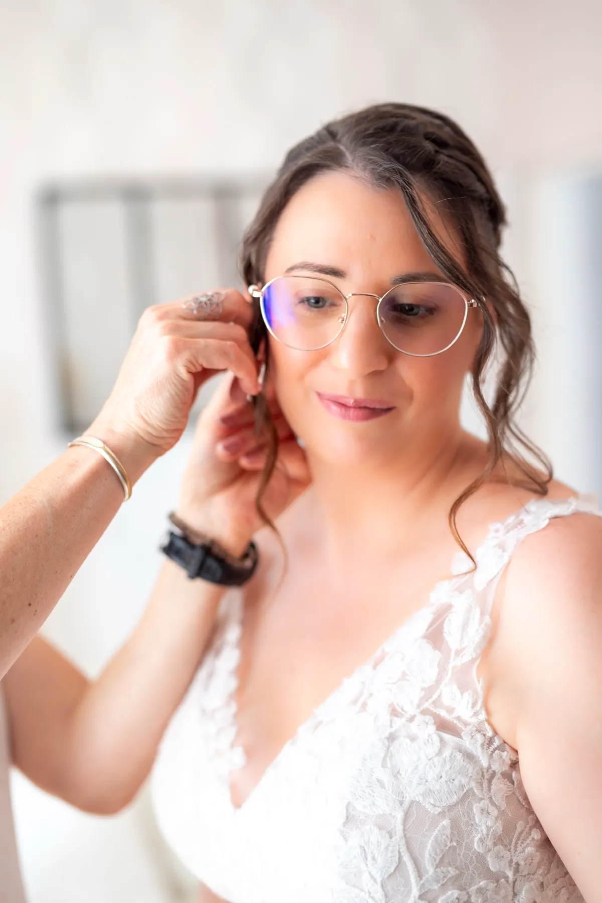 La mariée, en robe de dentelle et lunettes, attache sa boucle d’oreille