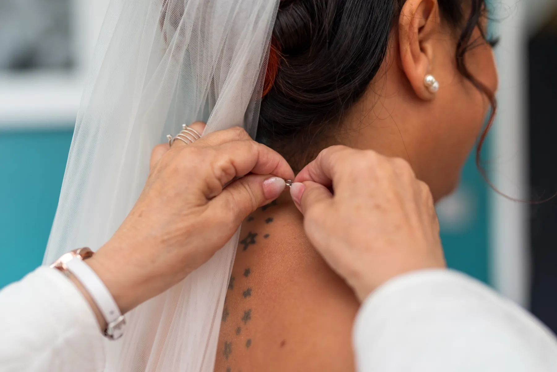 Gros plan sur deux mains qui ferment le collier de la mariée, sous le voile