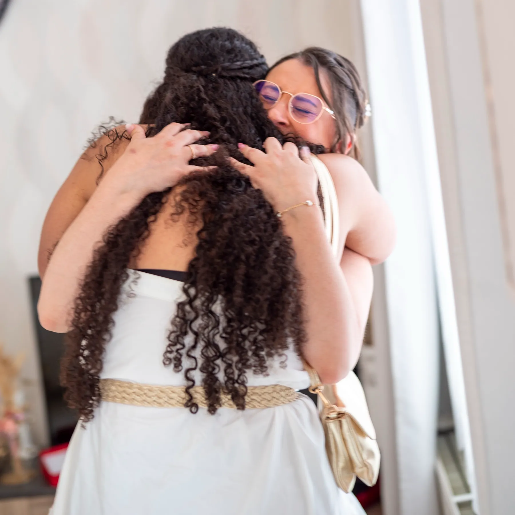 La mariée serre dans ses bras une invitée aux longs cheveux bouclés