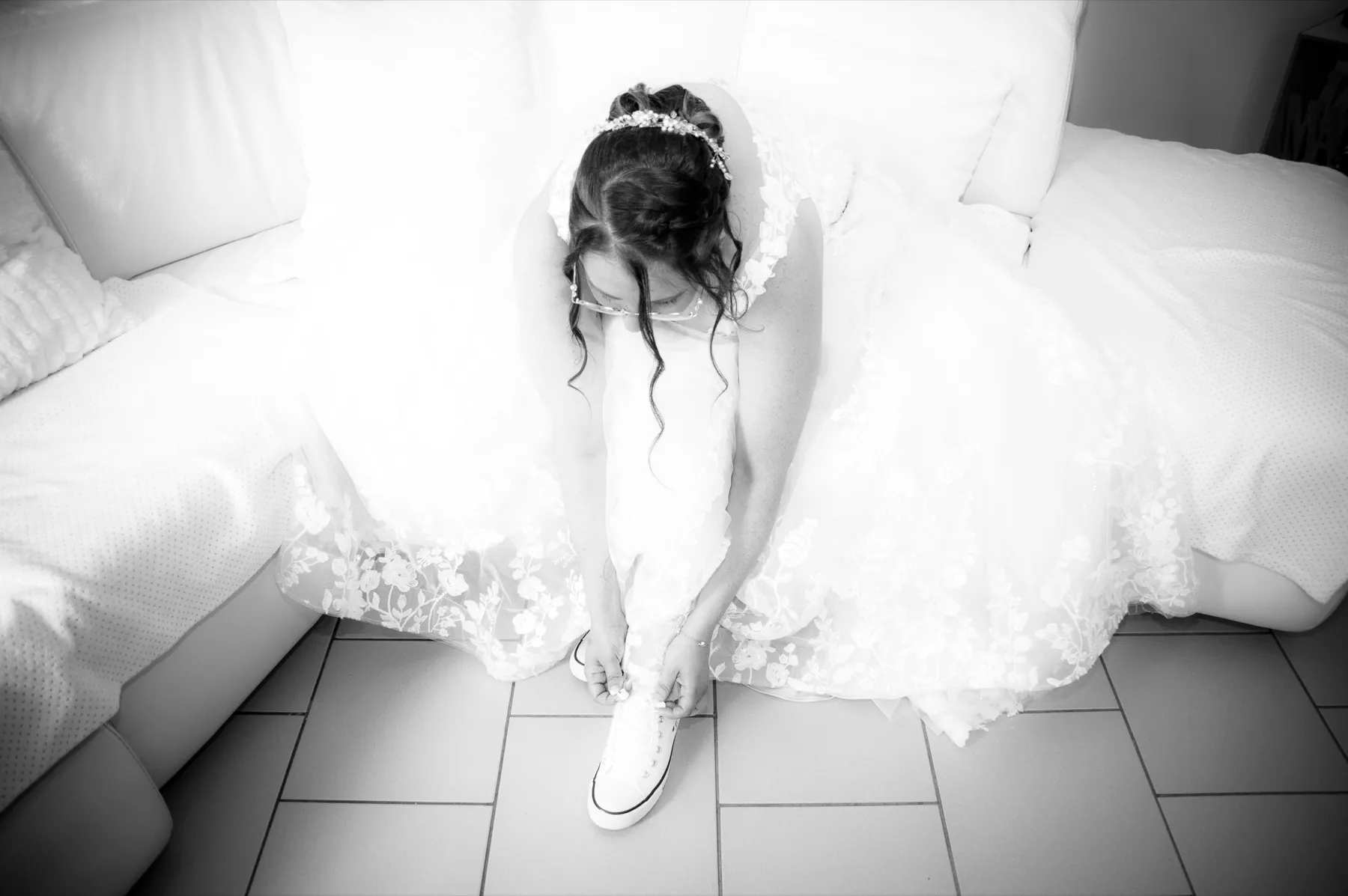 En noir et blanc, la mariée assise dans sa robe enfile ses chaussures