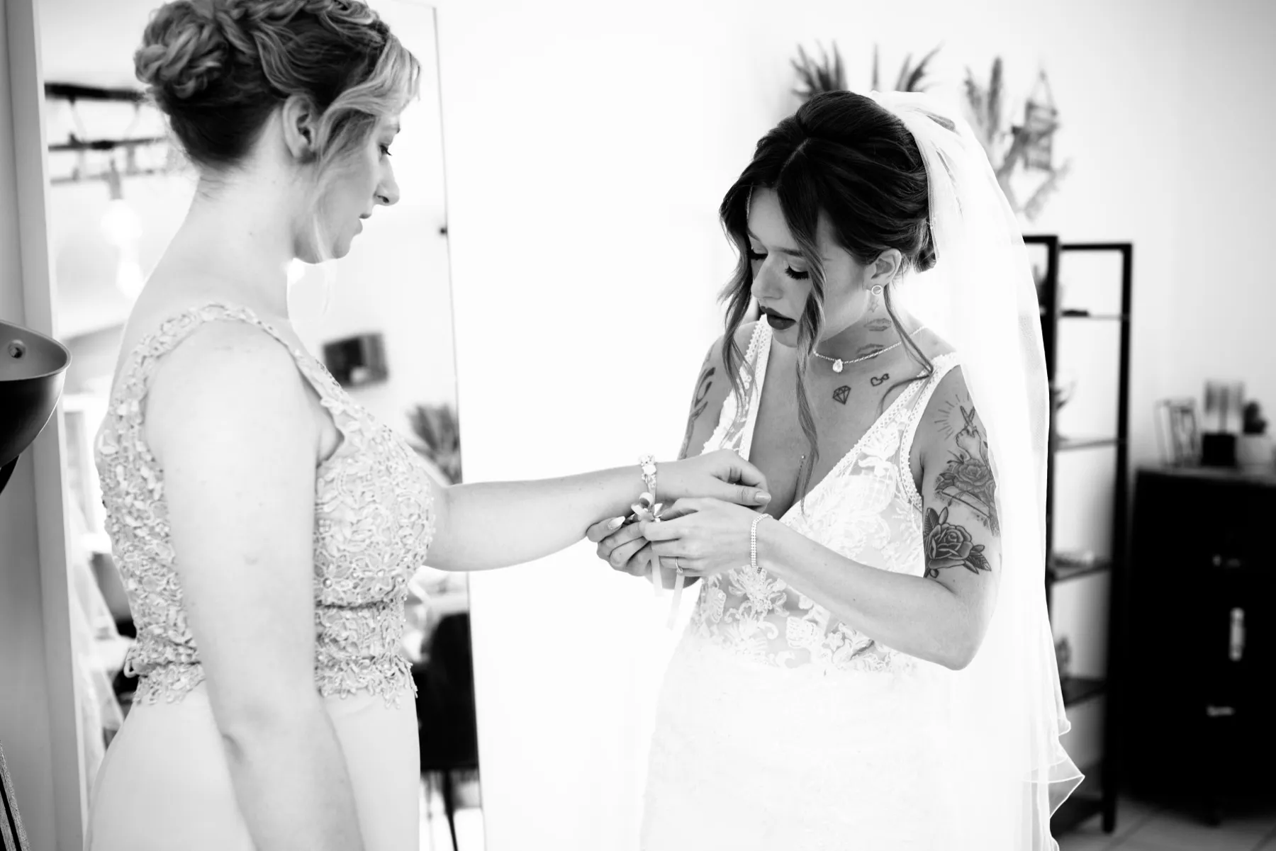 En noir et blanc, une proche attache un bracelet au poignet de la mariée