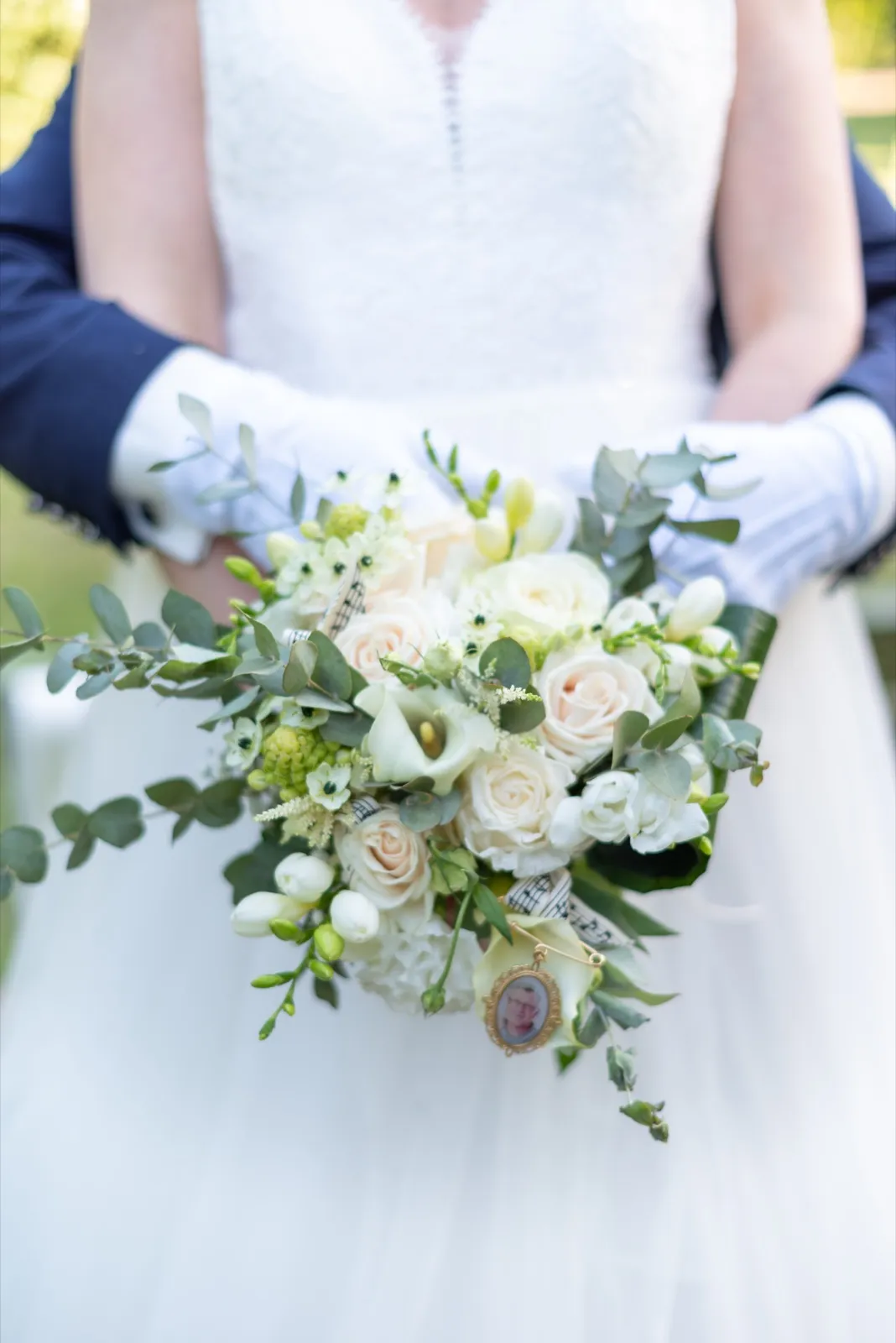 Bouquet blanc aux roses et feuillage, tenu devant la robe, avec des gants blancs et un médaillon