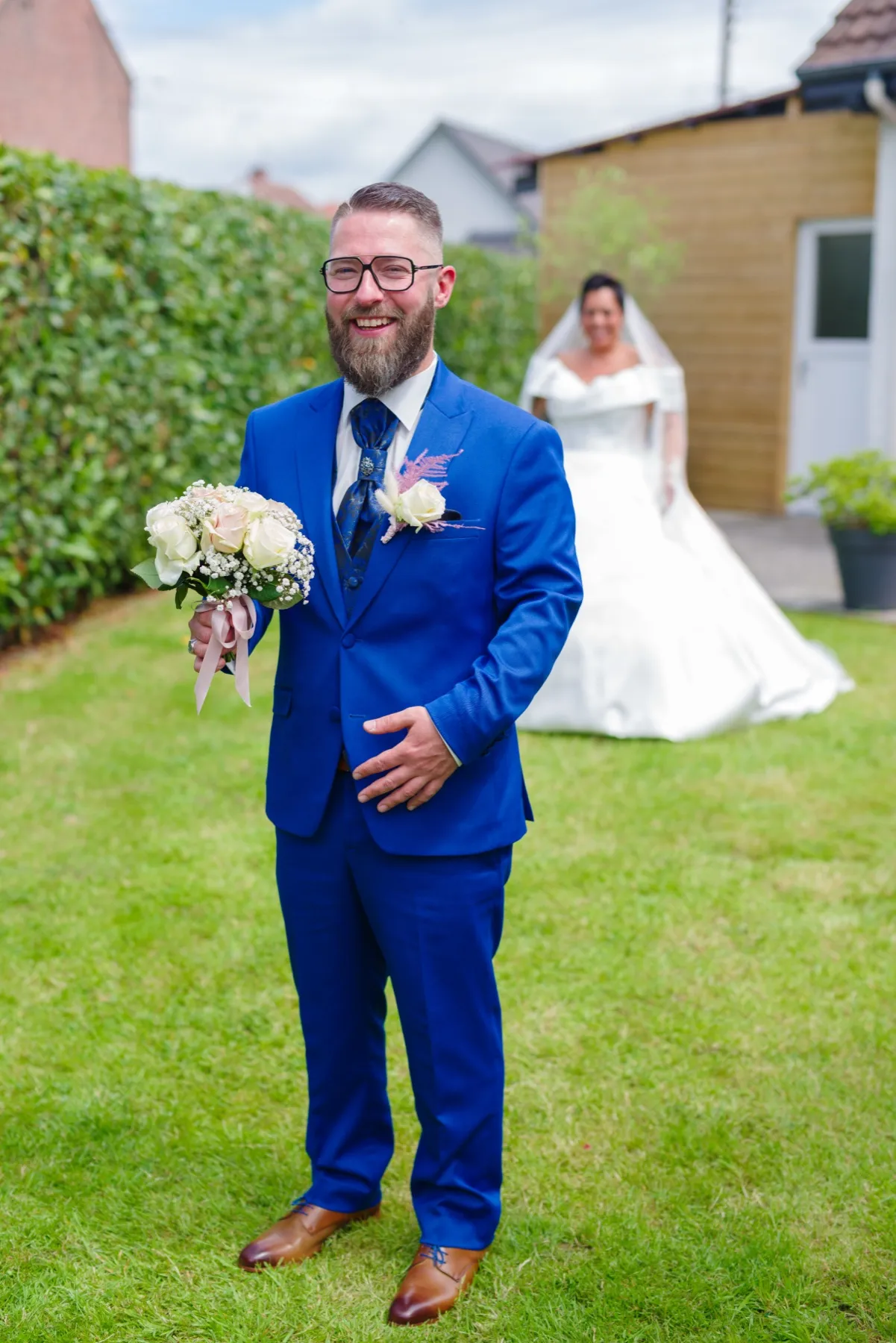 Le marié attend, le bouquet à la main, pendant que la mariée s’approche derrière lui
