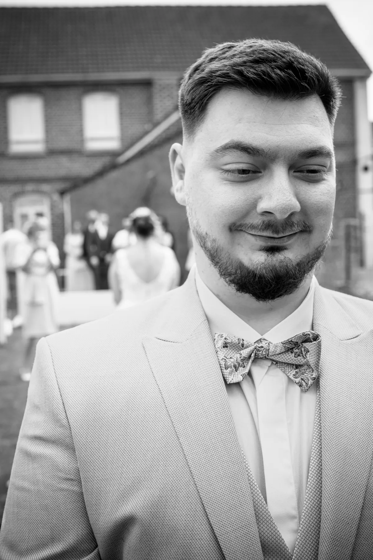 En noir et blanc, le marié en costume clair attend, les yeux baissés