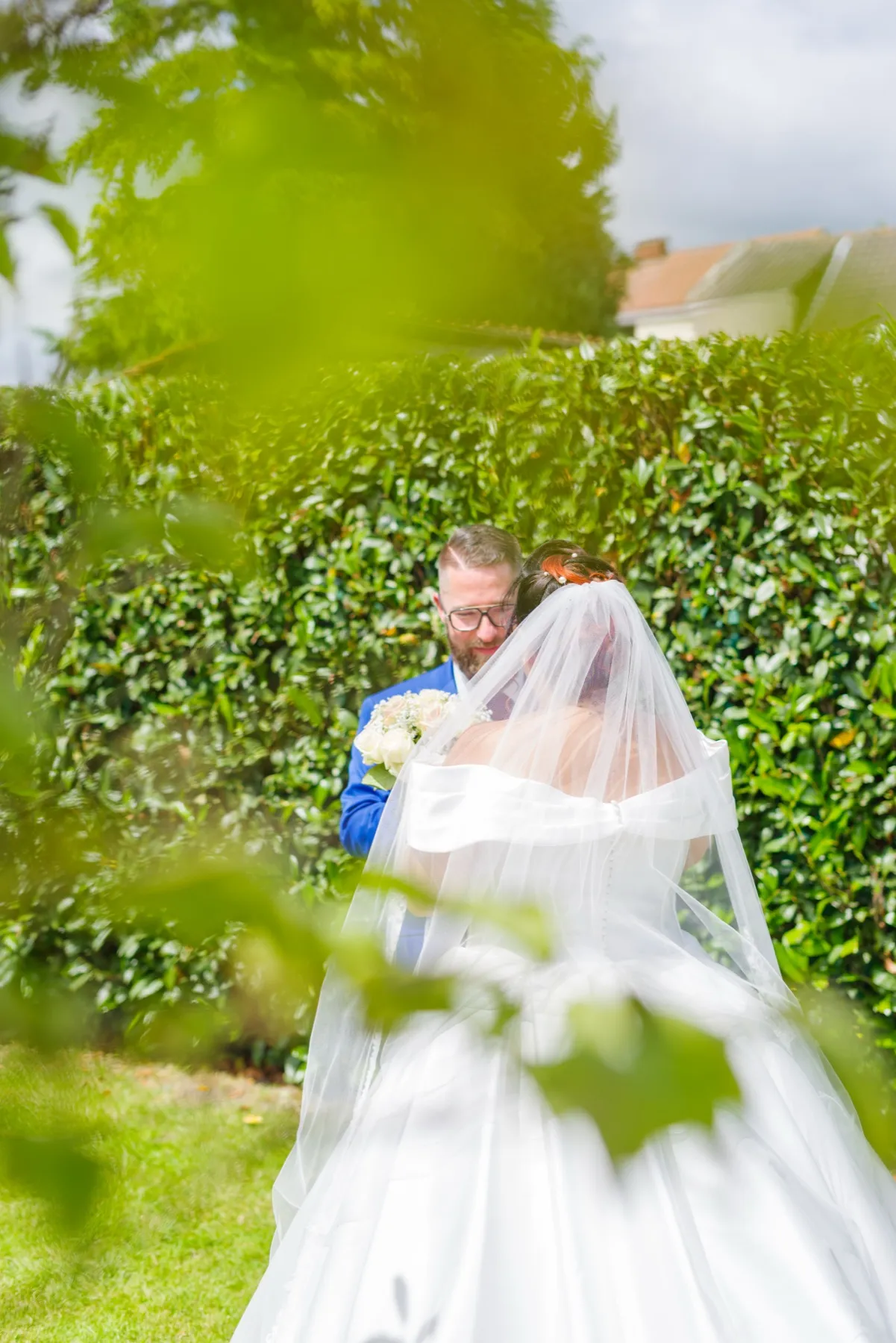 À travers les feuilles, le marié embrasse le front de la mariée sous son voile