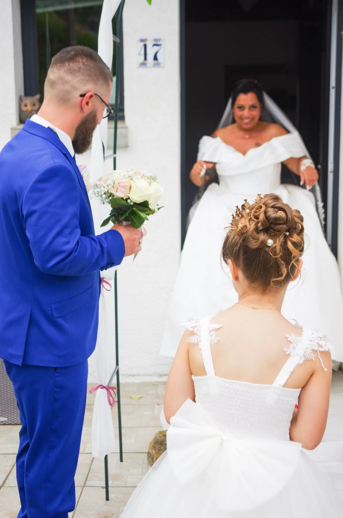 Vus de dos, le marié et une petite fille regardent la mariée franchir la porte
