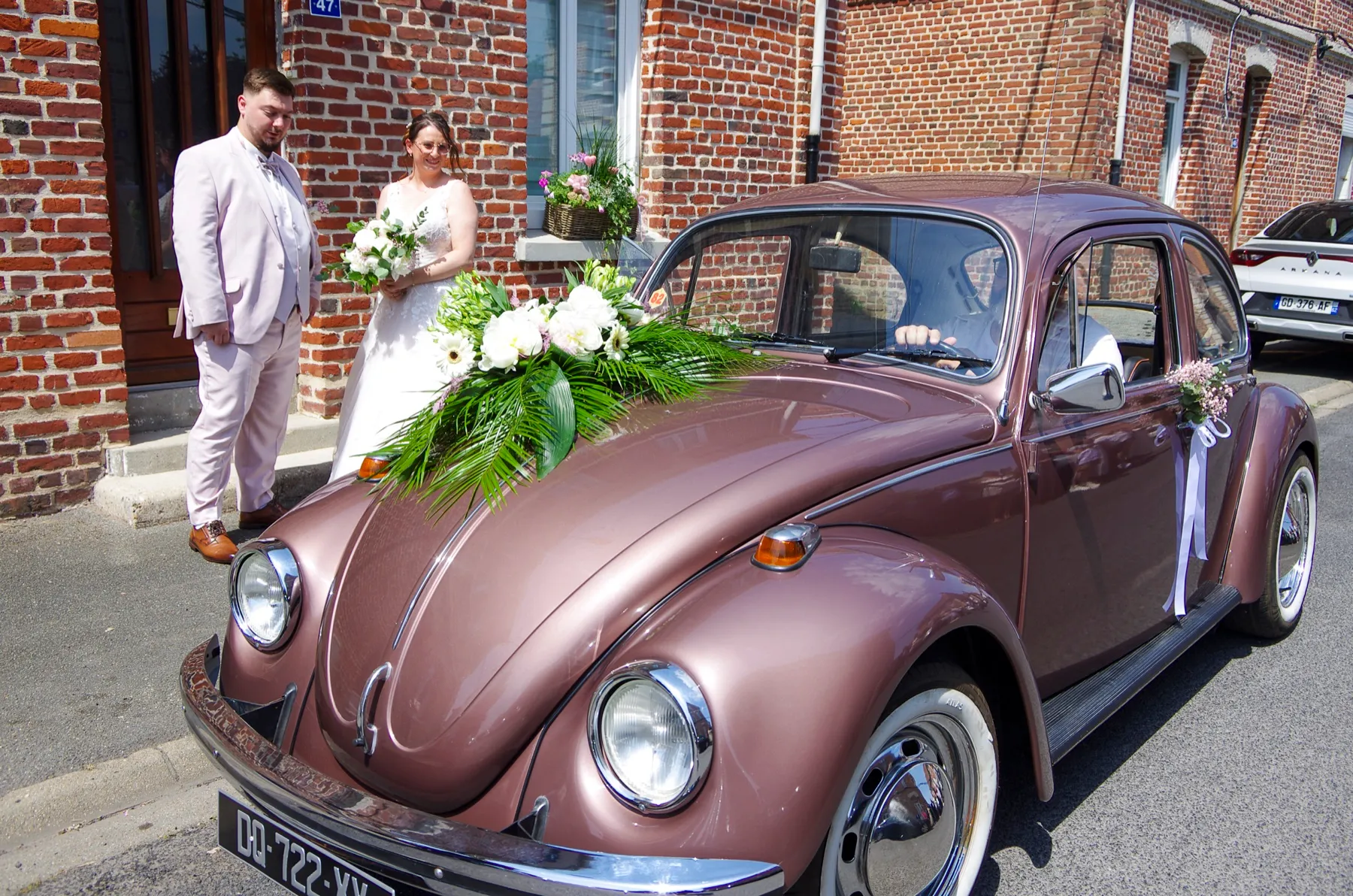 Les mariés derrière la Coccinelle vieux rose, un bouquet blanc sur le capot