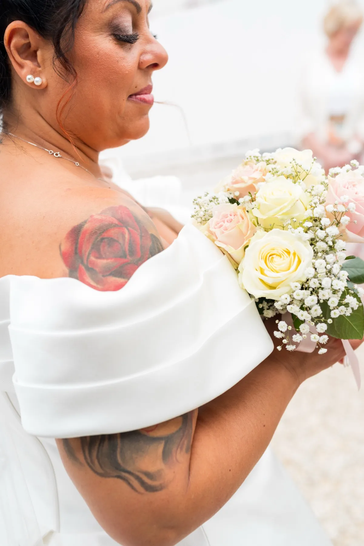 La mariée de profil, les yeux baissés sur son bouquet de roses, une rose tatouée sur l’épaule