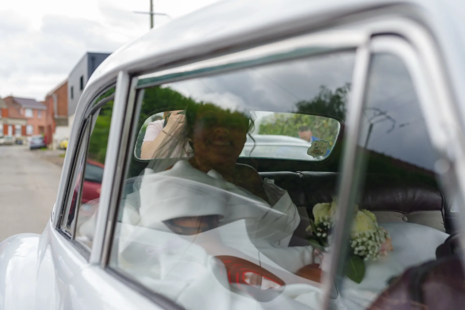 La mariée et son bouquet aperçus à travers la vitre arrière d’une voiture ancienne