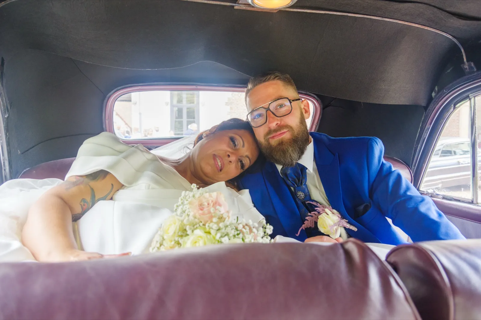Allongée sur la banquette d'une voiture ancienne, la mariée pose la tête contre l'épaule du marié