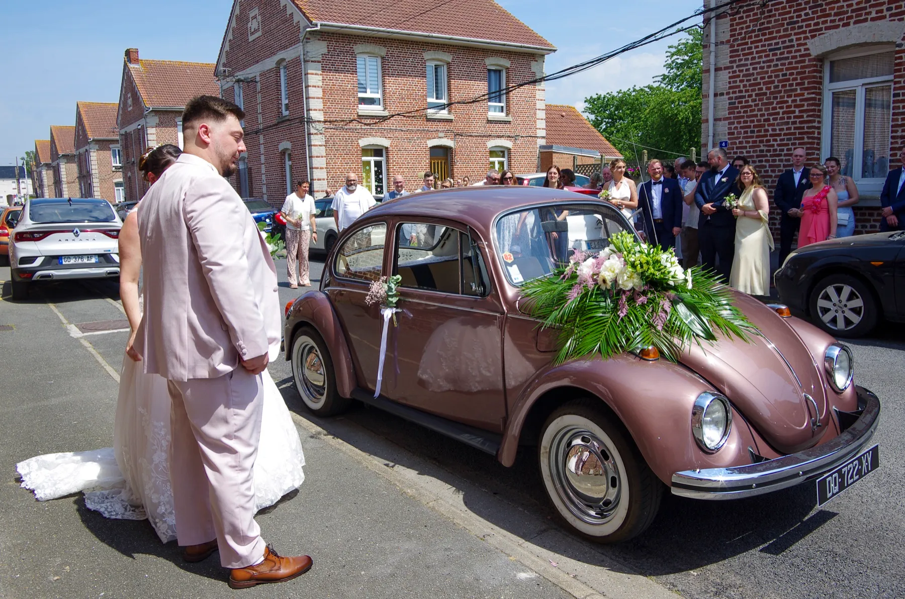 Le marié en costume rose pâle près de la Coccinelle fleurie, dans la rue