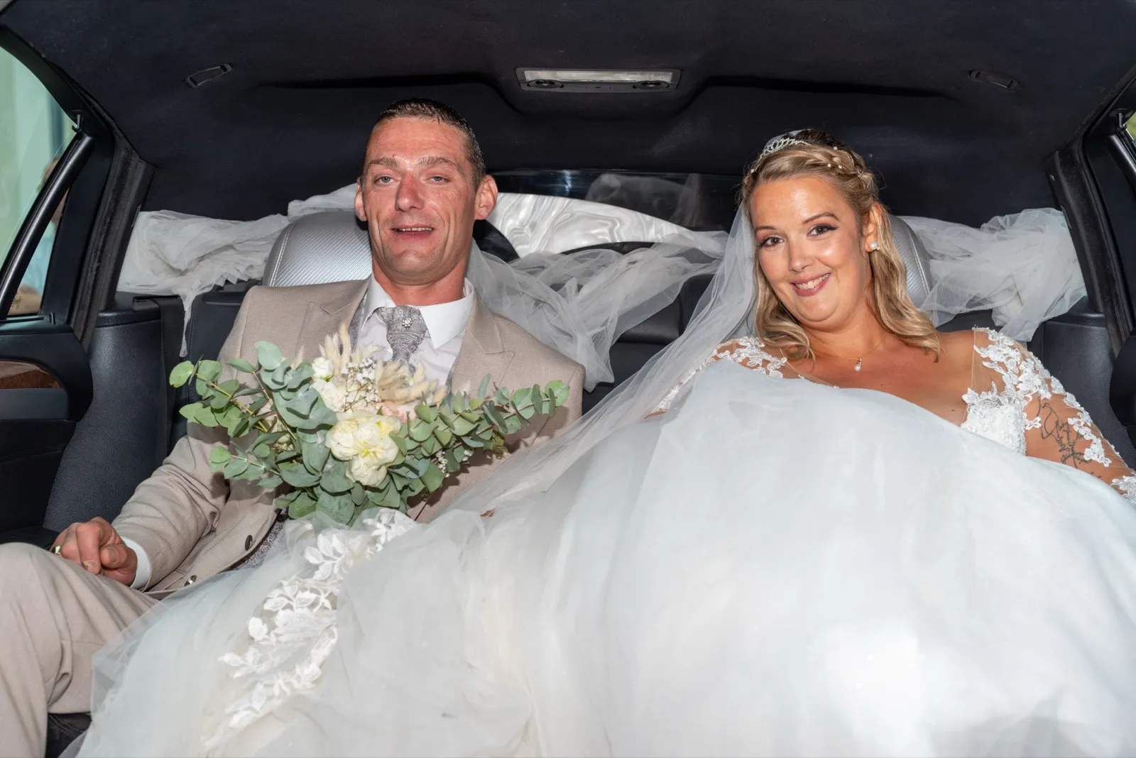 Les mariés sourient dans une voiture, le voile de la mariée flottant derrière eux