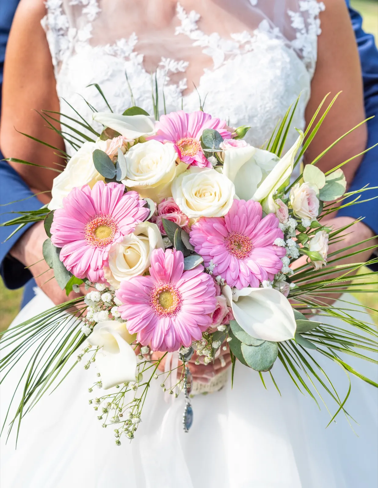 Bouquet de gerberas roses et de roses blanches serré contre la robe de la mariée