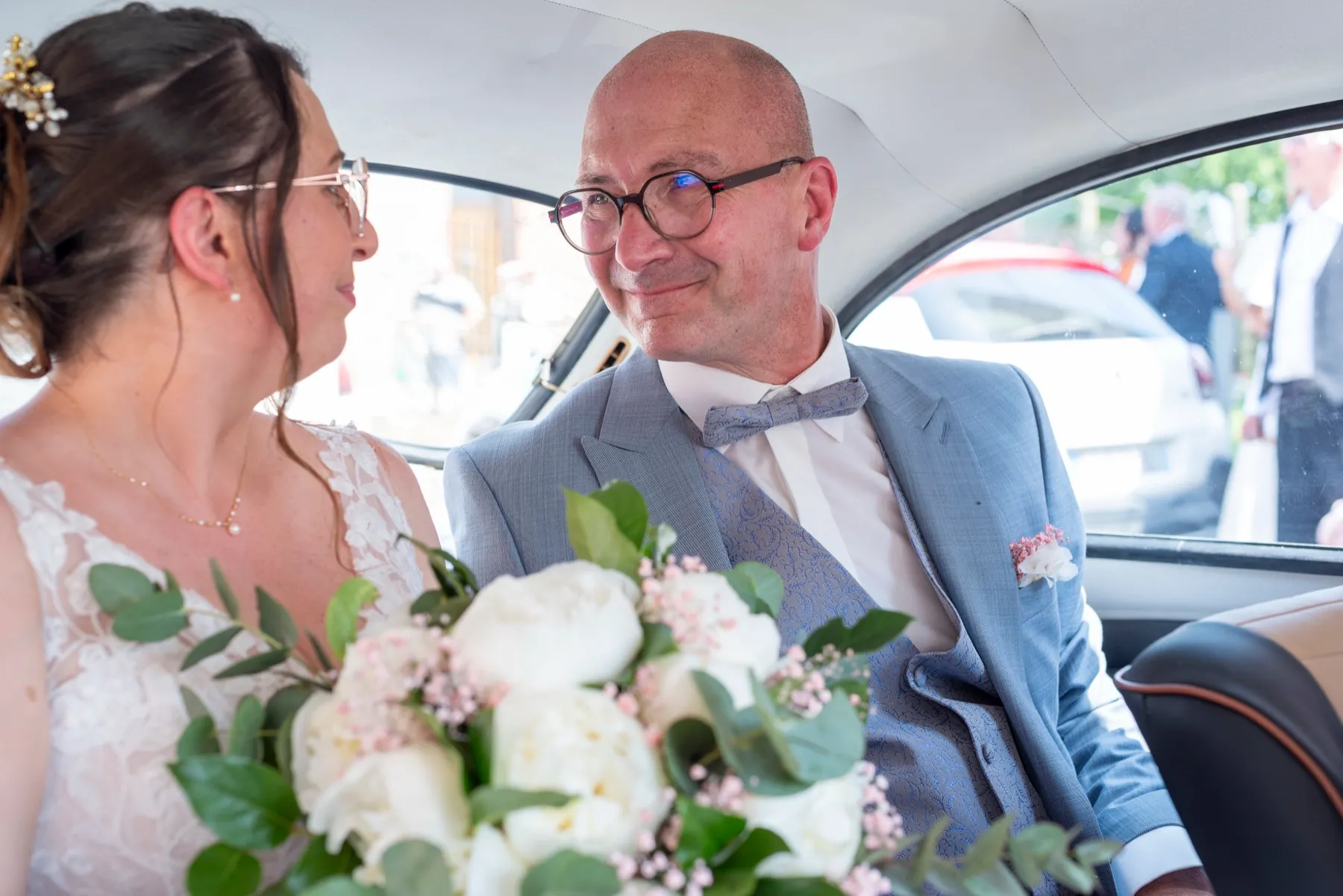 Dans la Coccinelle, la mariée et son papa échangent un regard, le bouquet entre eux