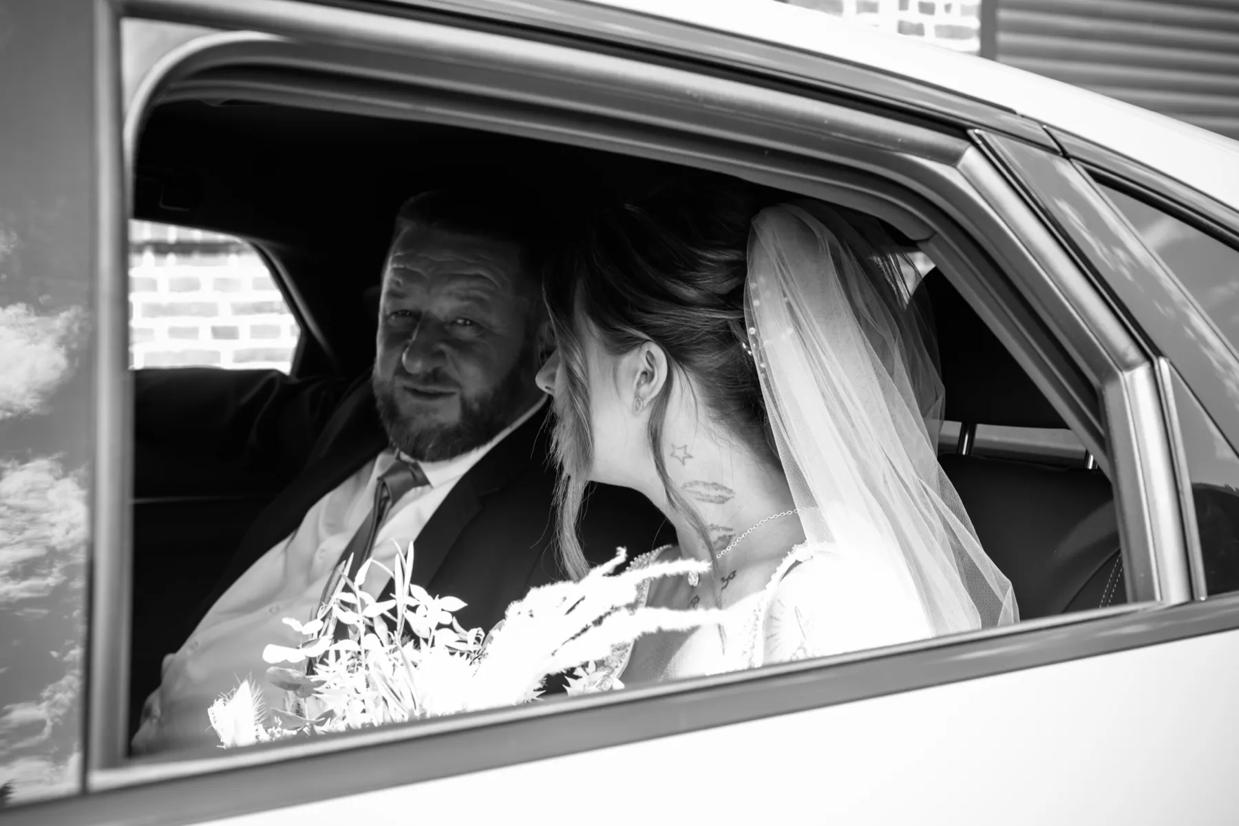 En noir et blanc, la mariée dans la voiture, tournée vers l’homme assis à côté d’elle