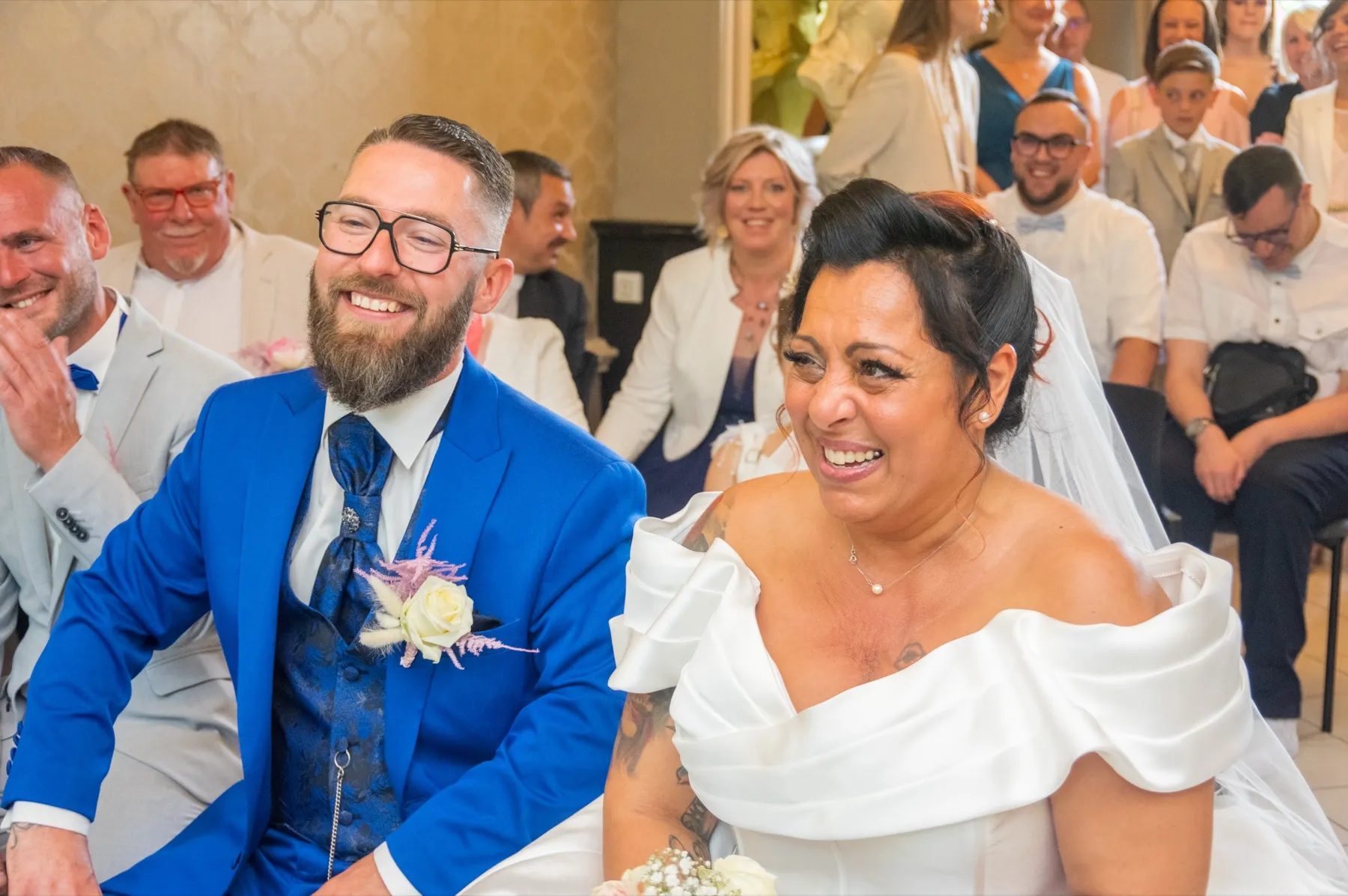Assis côte à côte à la mairie, les mariés éclatent de rire au milieu de leurs invités