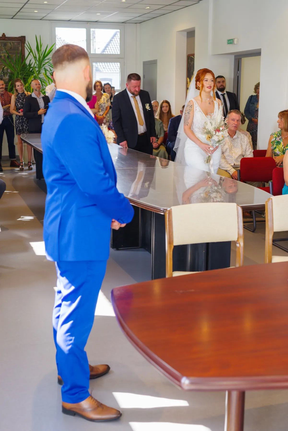 Vu de dos, le marié regarde la mariée entrer dans la salle des mariages