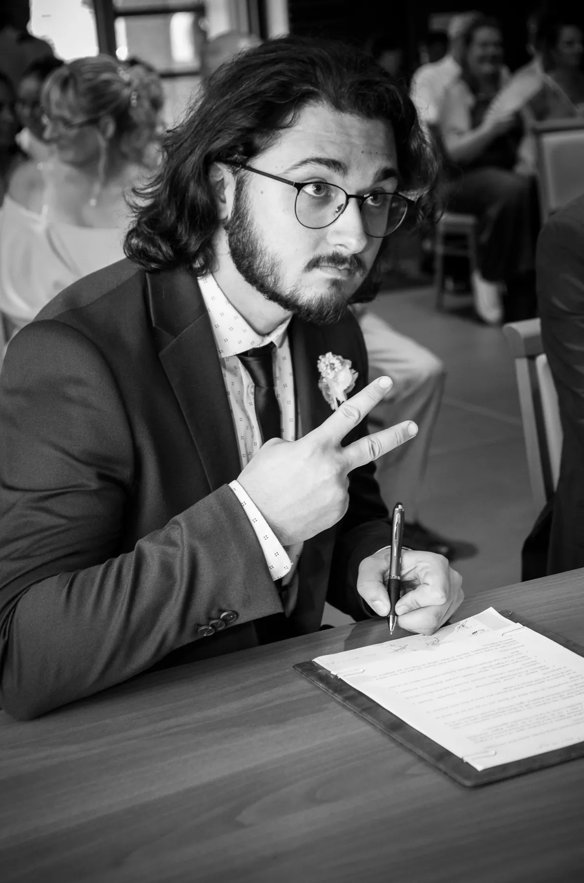 En noir et blanc, un invité à lunettes fait le signe de la victoire en signant le registre