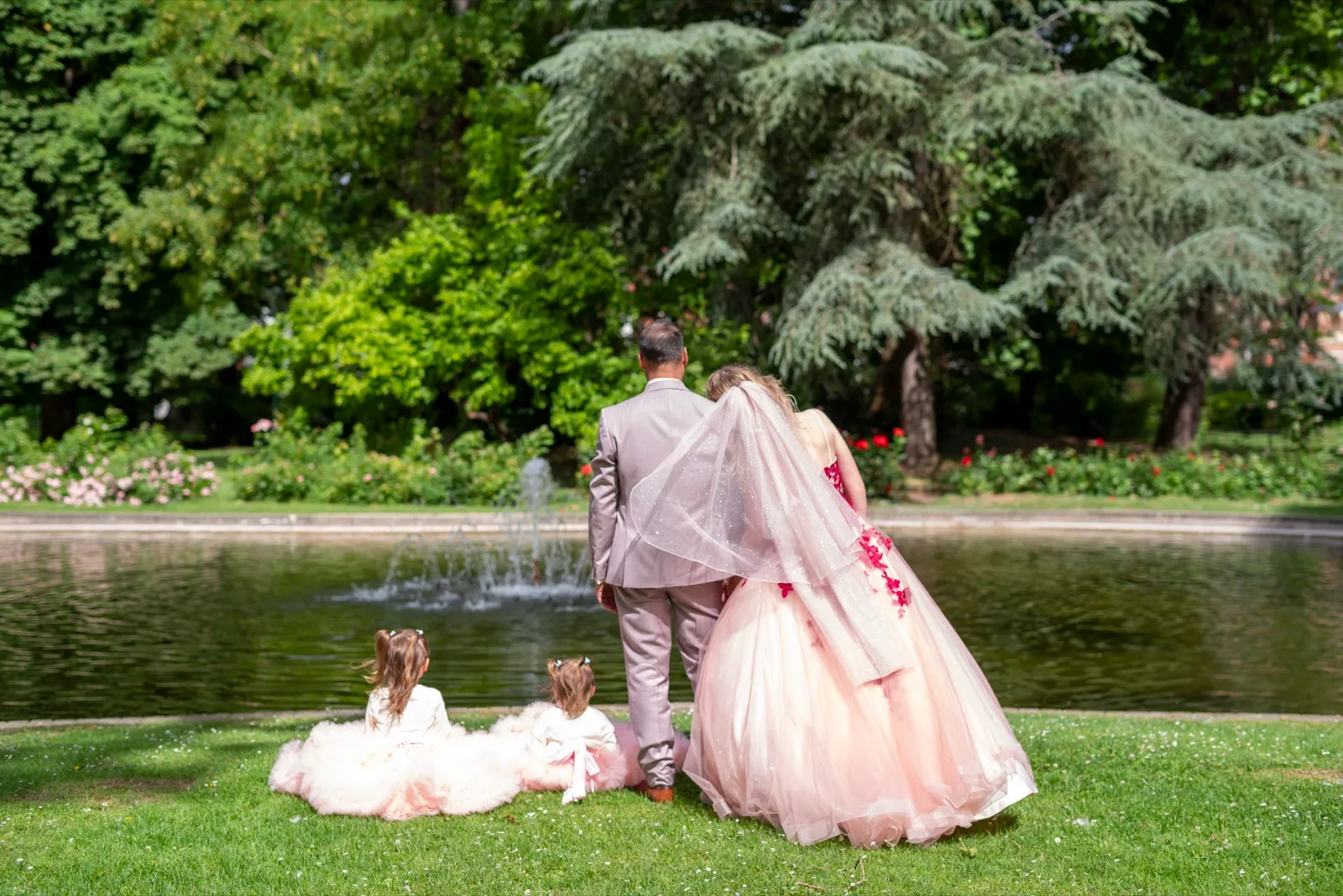 De dos au bord d'un bassin, les mariés regardent la fontaine, deux petites filles assises à leurs pieds