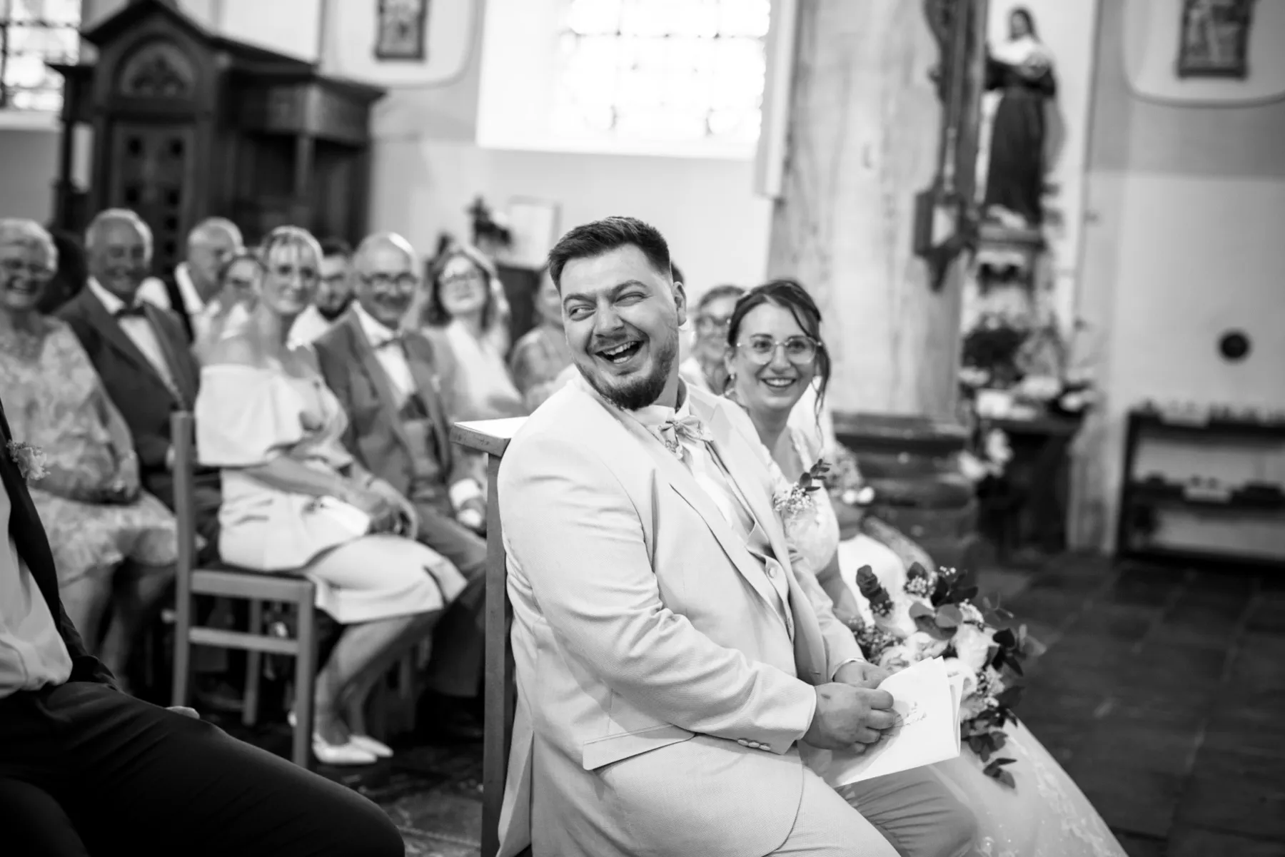 En noir et blanc, les mariés assis éclatent de rire pendant la cérémonie