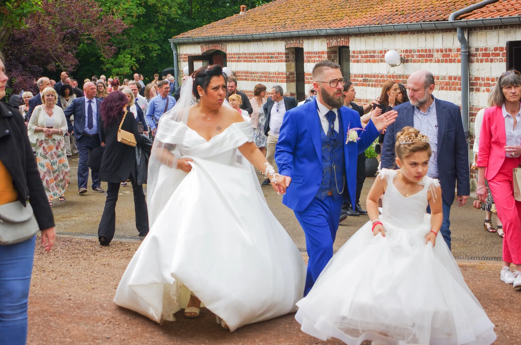 Les mariés marchent main dans la main parmi leurs invités, une petite fille en robe blanche devant eux