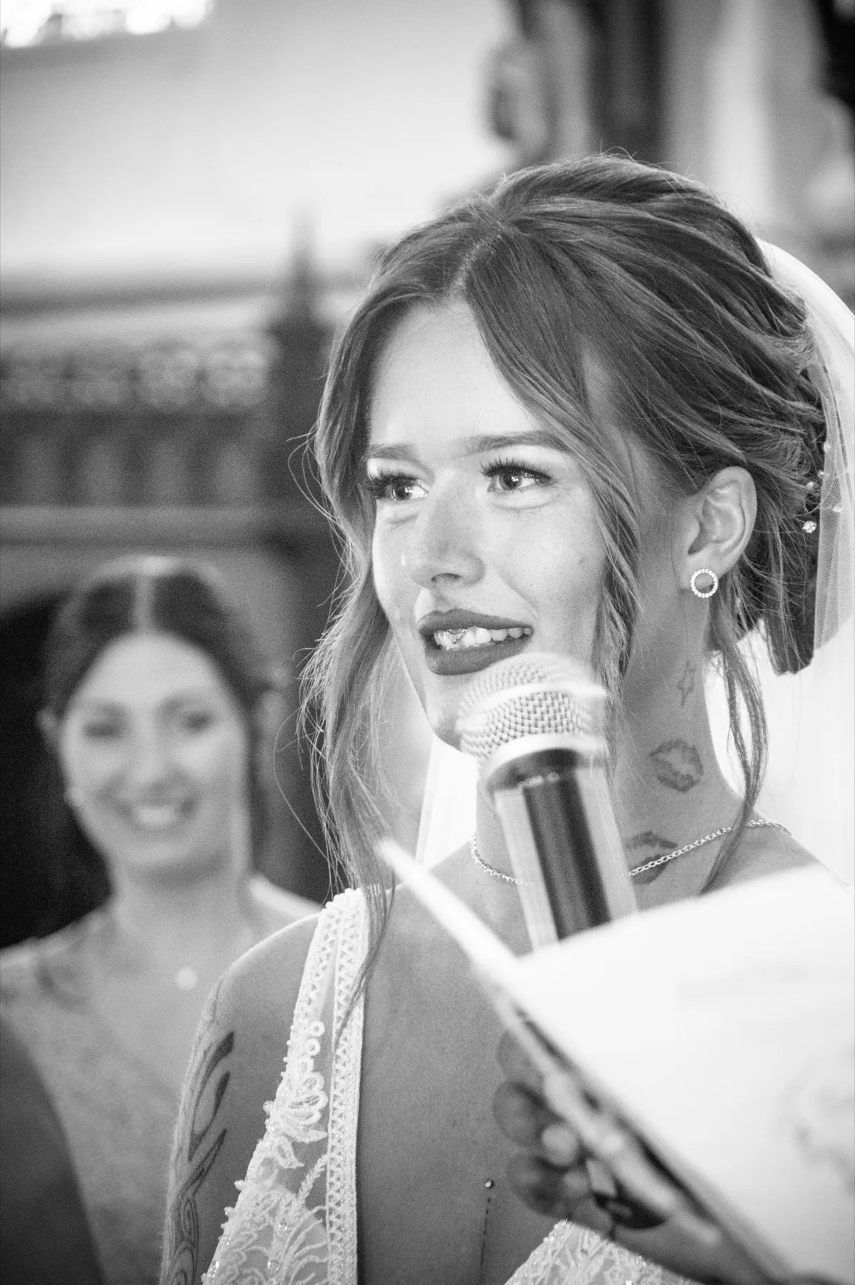En noir et blanc, la mariée, émue, parle au micro pendant la cérémonie