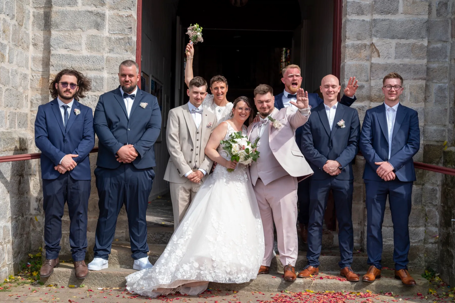 Les mariés et leurs témoins en costume bleu marine devant la porte de l’église
