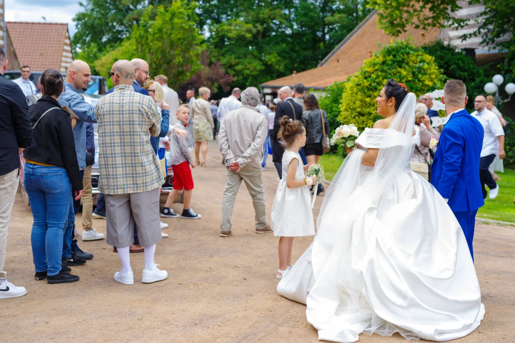 Les mariés de dos, entourés d’invités dans la cour, devant un jardin