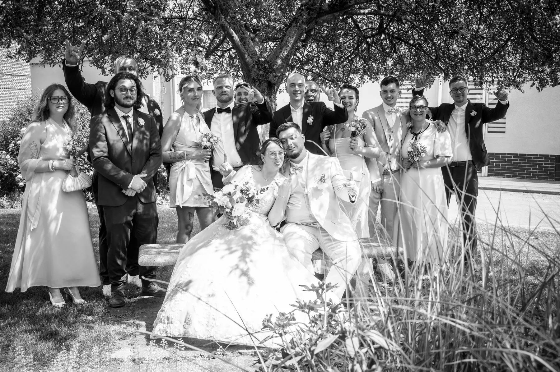 En noir et blanc, les mariés et leurs proches rient sous un arbre