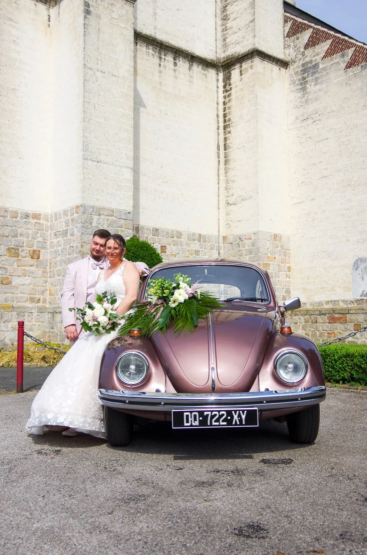 Les mariés près de la Coccinelle vieux rose, au pied du mur de pierre de l’église