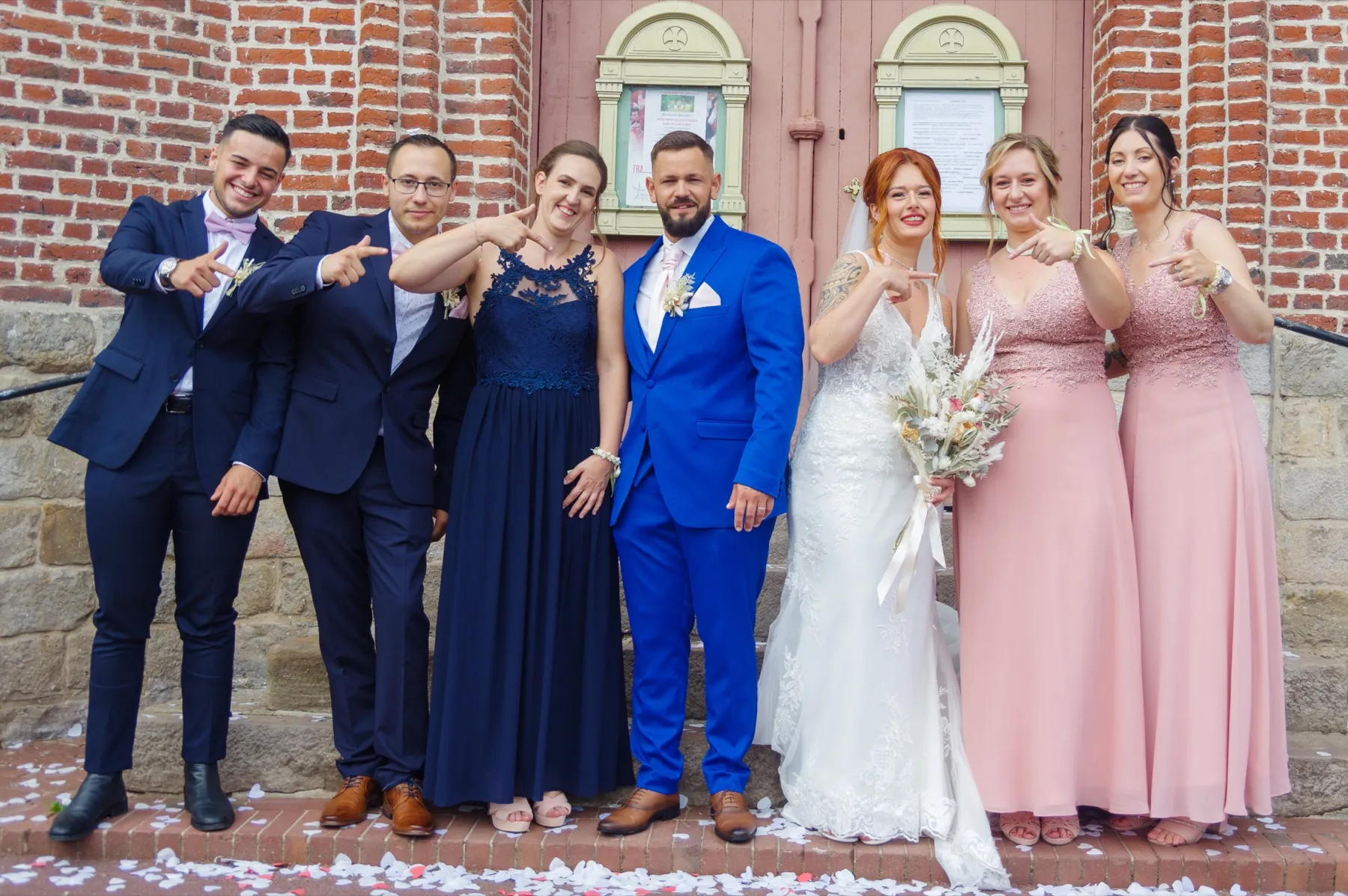 Les mariés posent avec cinq proches, en bleu marine et en rose, devant l’église
