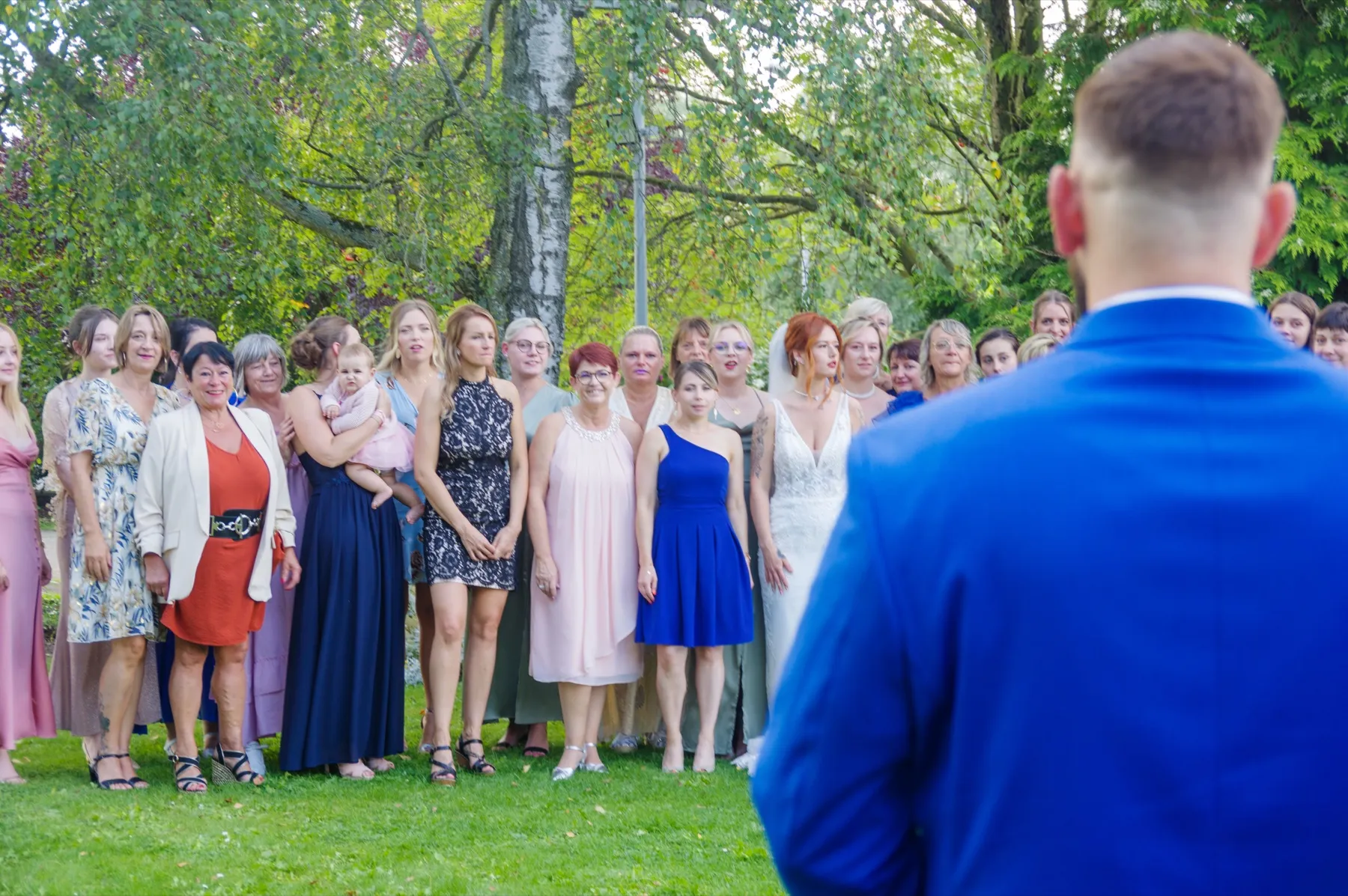 Le marié, de dos au premier plan, fait face aux invitées réunies autour de la mariée