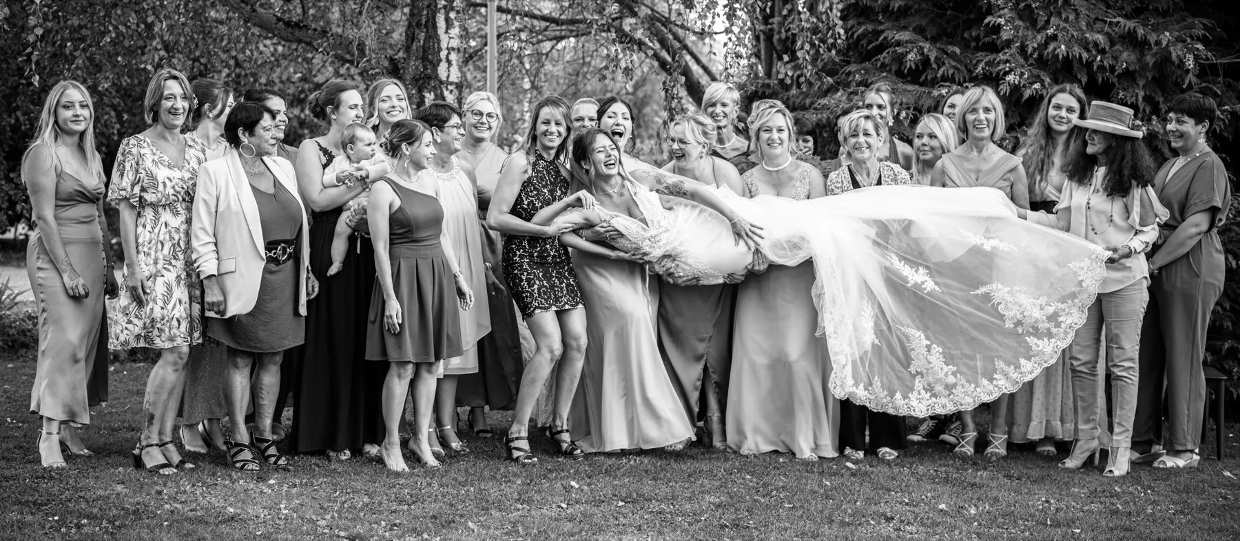 En noir et blanc, les invitées portent la mariée à l’horizontale, sa traîne déployée