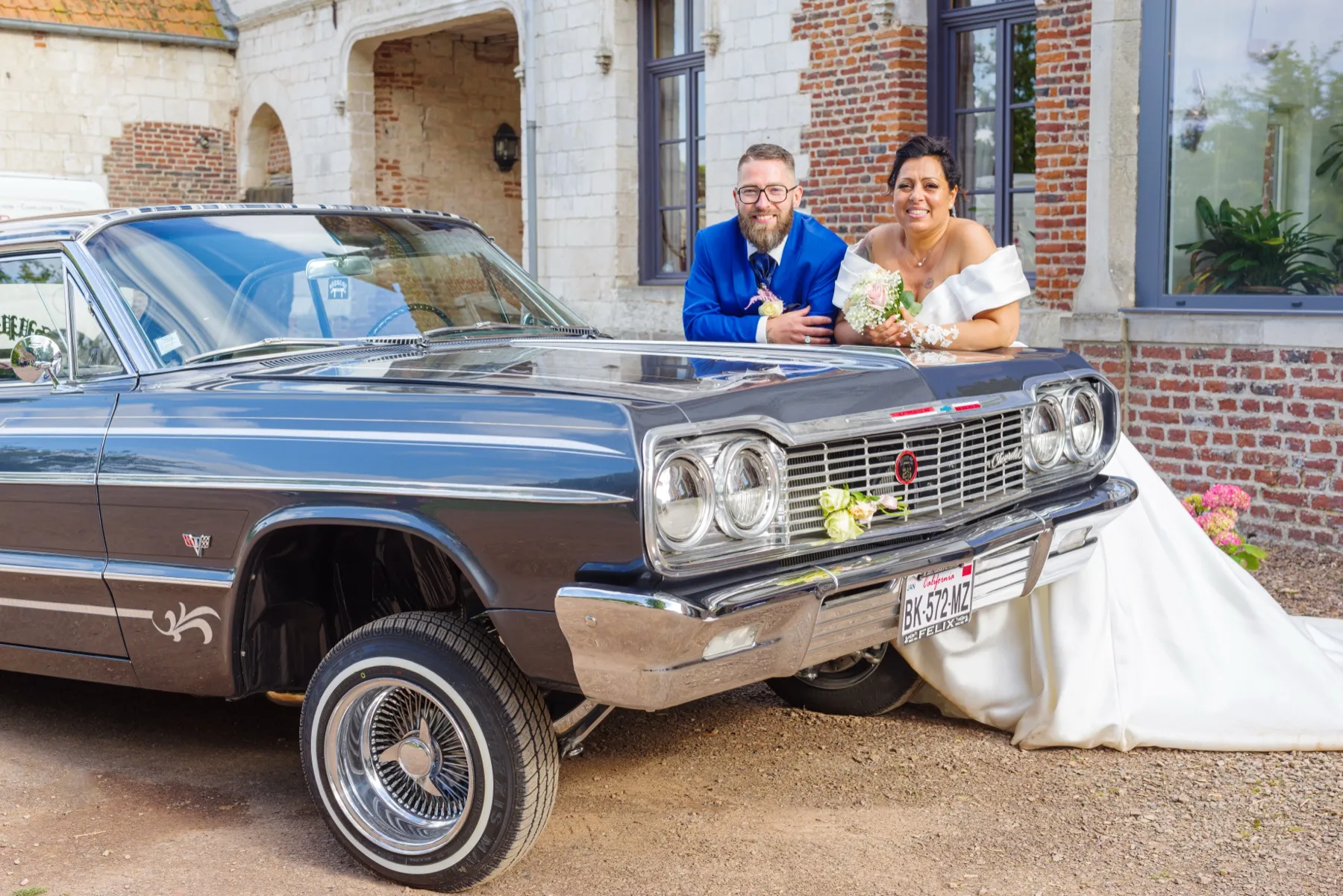 Les mariés accoudés au capot d’une voiture américaine ancienne, la robe étalée sur le sol