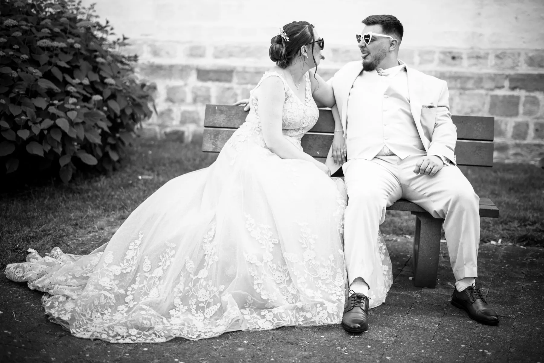 En noir et blanc, les mariés en lunettes de soleil assis sur un banc