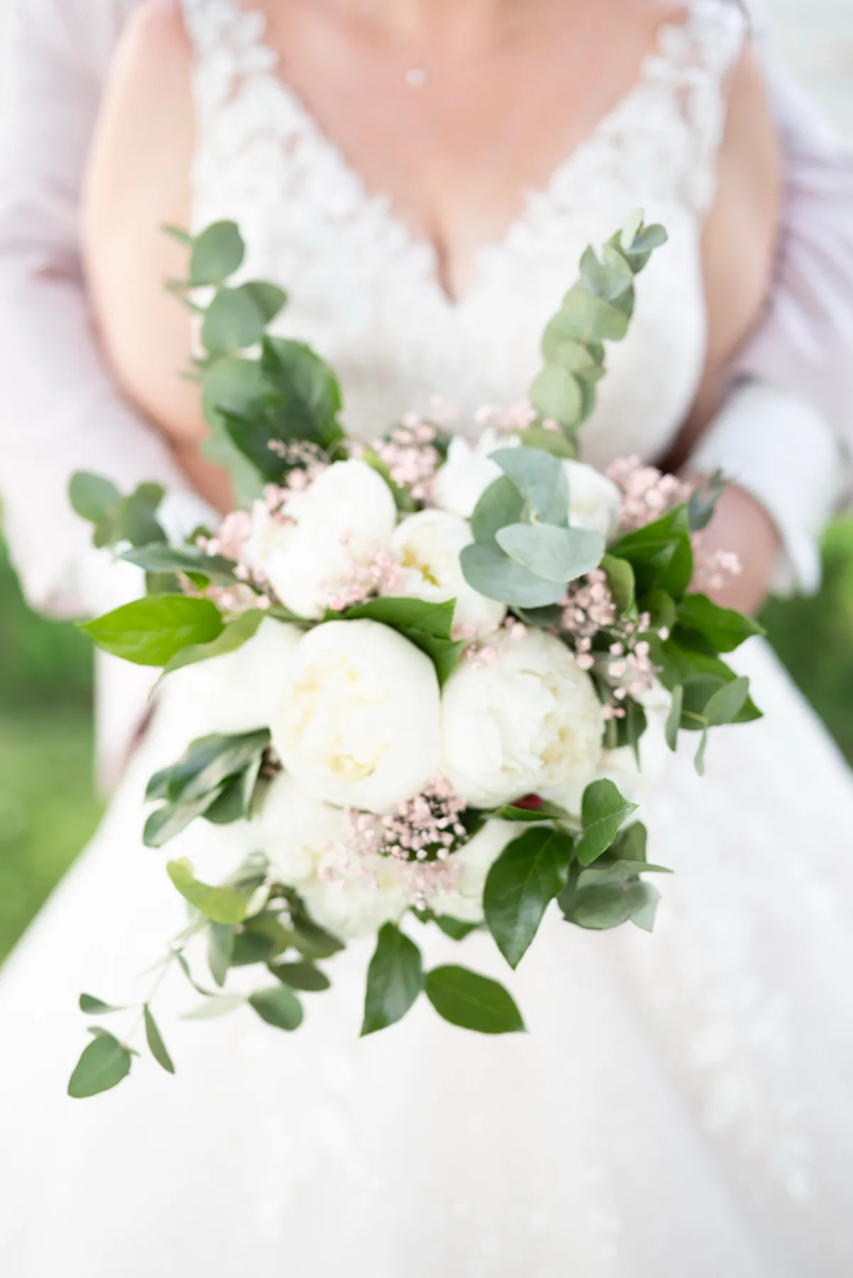 Gros plan sur le bouquet de pivoines blanches tenu contre la robe de dentelle