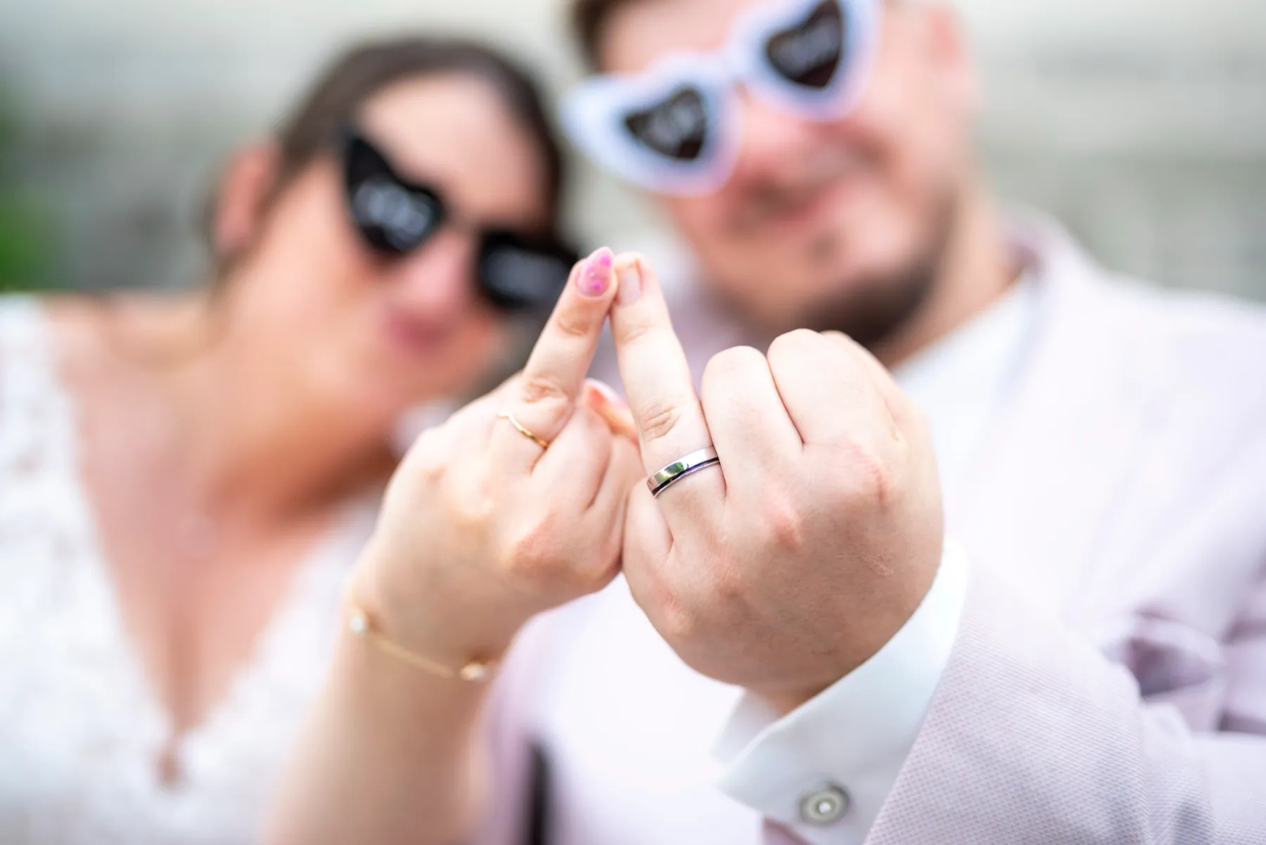 Les mariés en lunettes en cœur tendent leur annulaire pour montrer leurs alliances