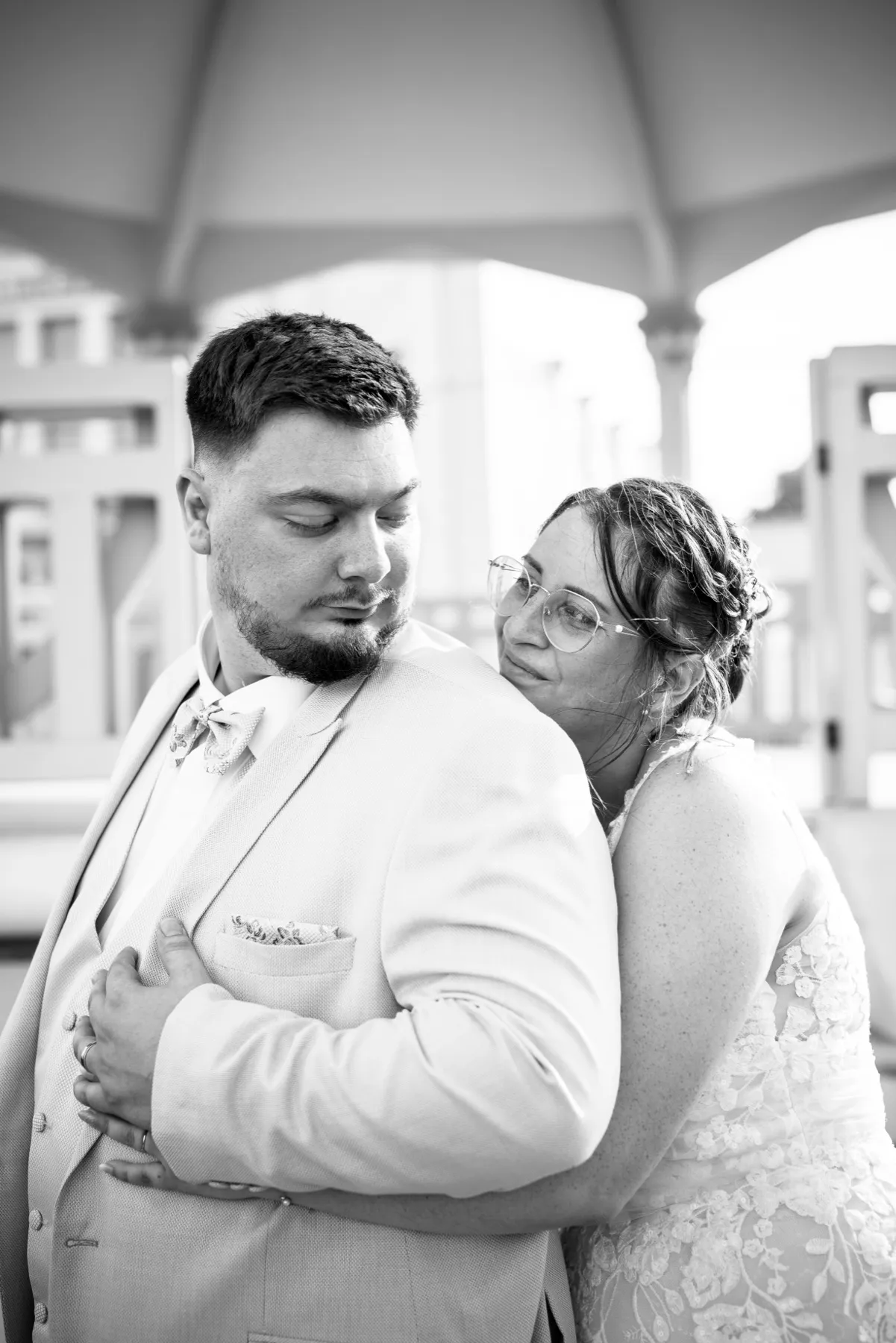 En noir et blanc, la mariée appuie sa tête contre l’épaule du marié, sous un kiosque
