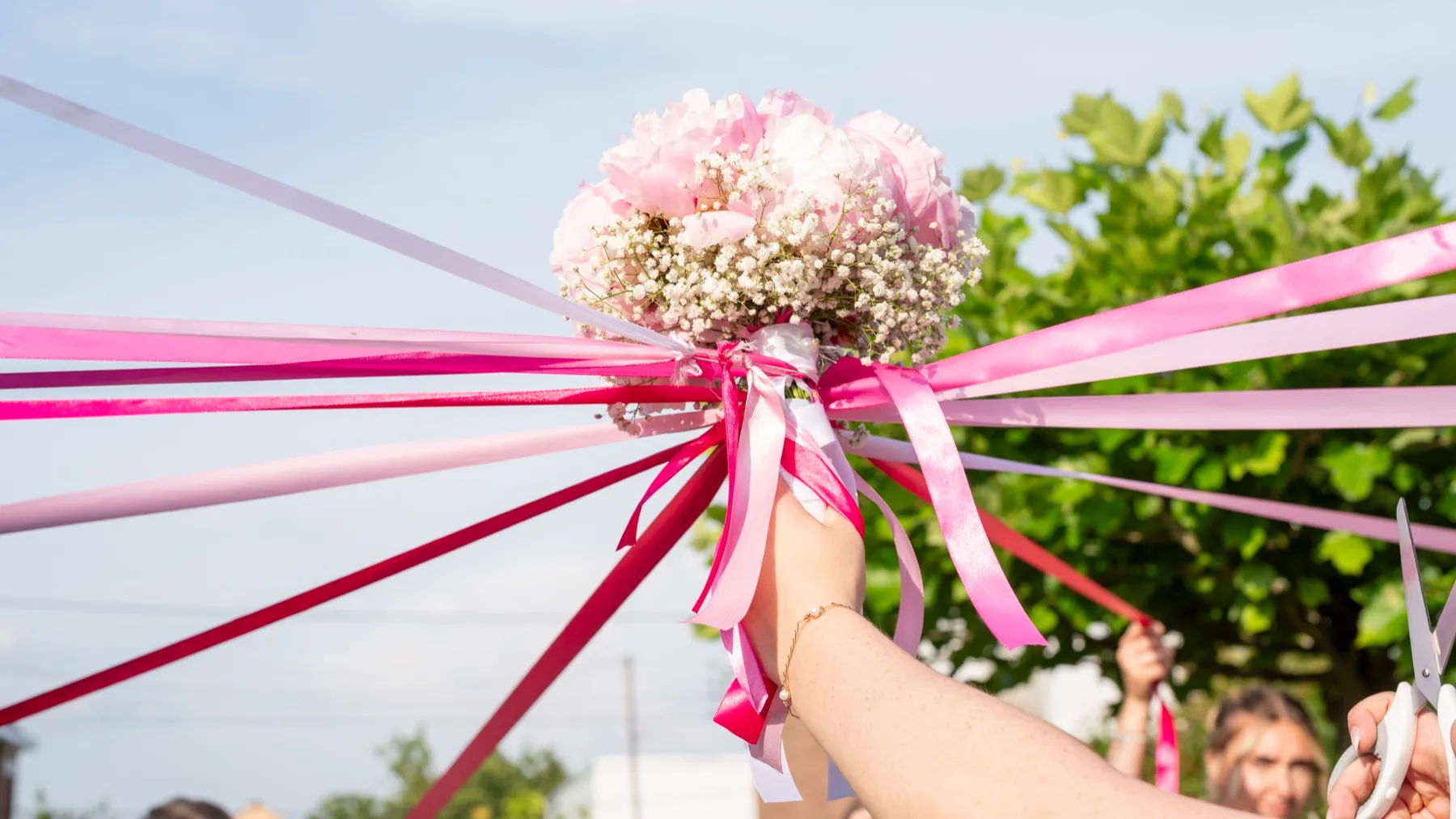 Le bouquet rose levé au ciel, d’où partent des rubans roses et fuchsia