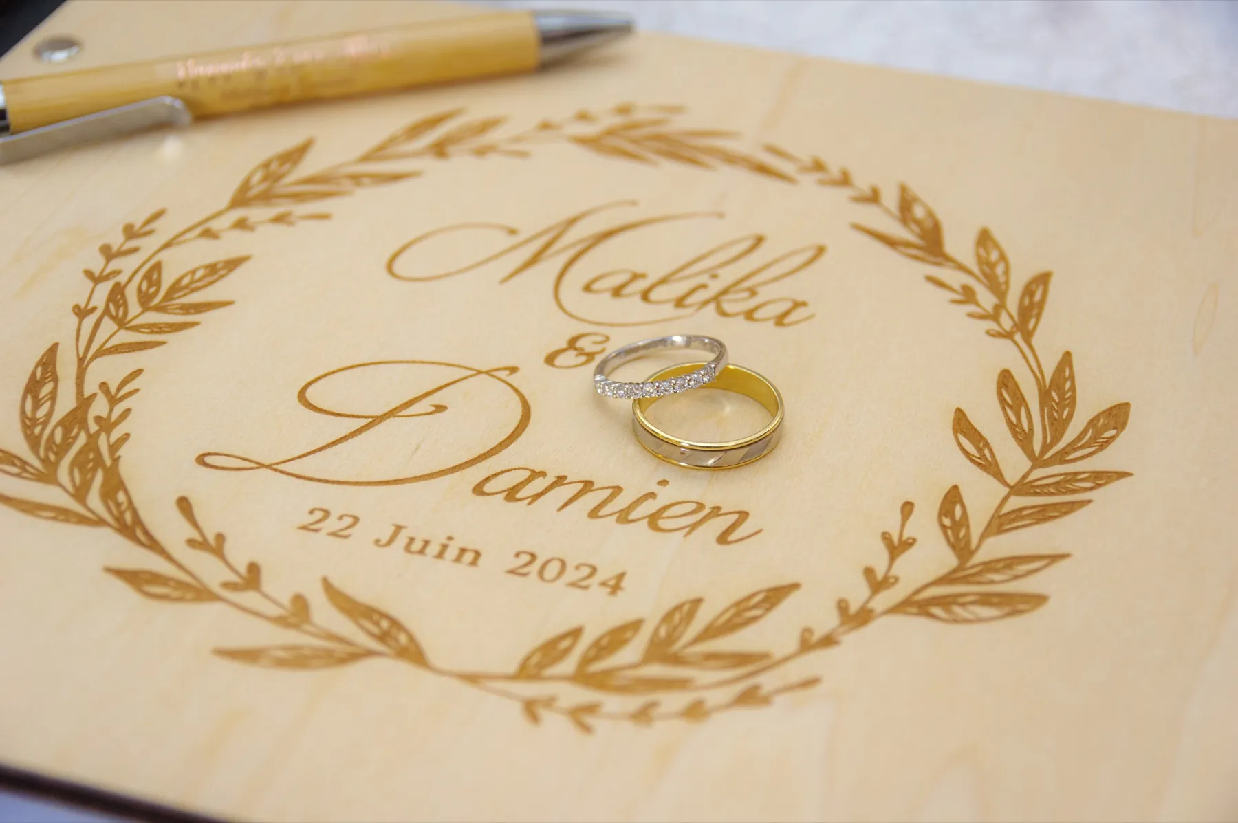 Les deux alliances posées sur le livre d’or en bois gravé « Malika & Damien, 22 juin 2024 »
